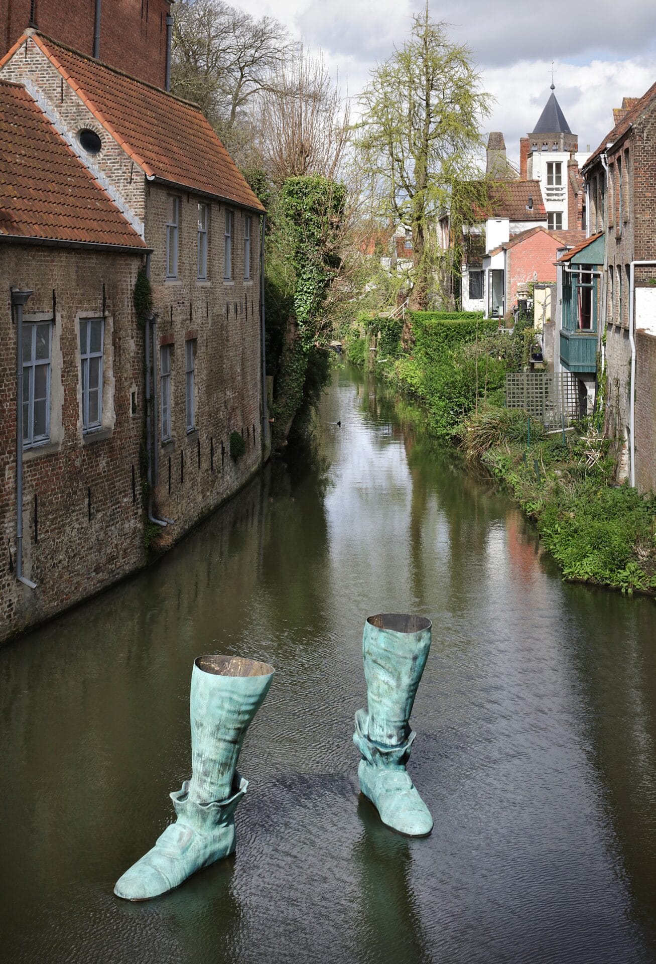 a sculpture of a pair of 18th-century style boots cast in bronze and installed in a Bruges canal