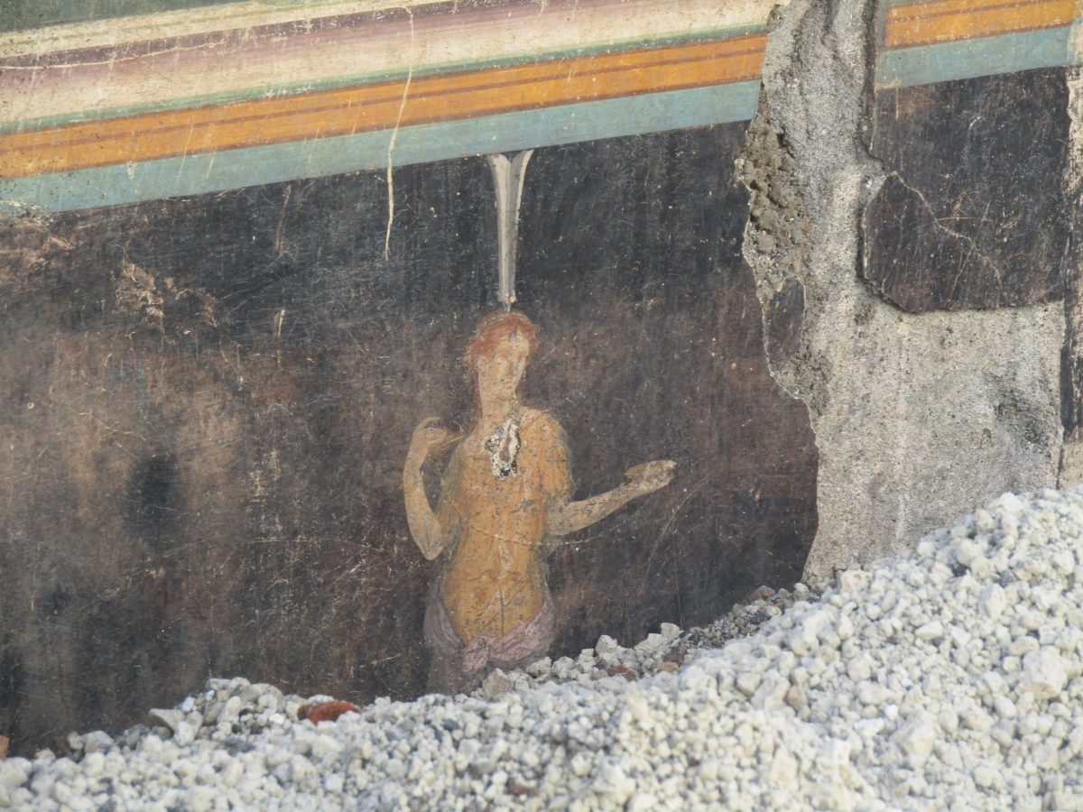 detail of a fresco in a Pompeii home's banquet room, showing an architectural border and a figure from Greek mythology, partly obscured under rubble