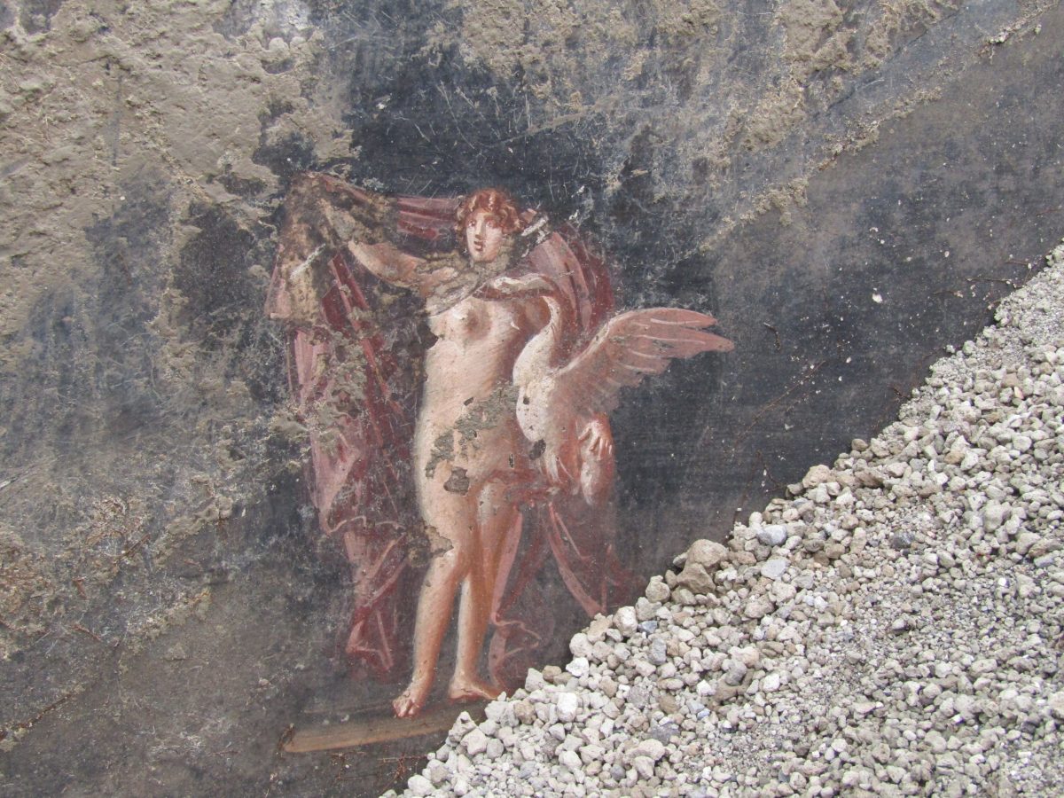 detail of a fresco partly obscured under rubble in a Pompeii home's banquet room, showing an architectural border and a figure from Greek mythology
