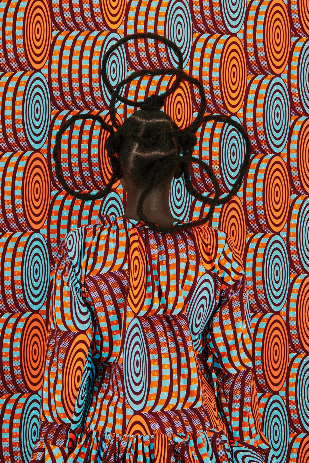 a portrait of the artist against a patterned orange and blue backdrop. her back is facing the camera