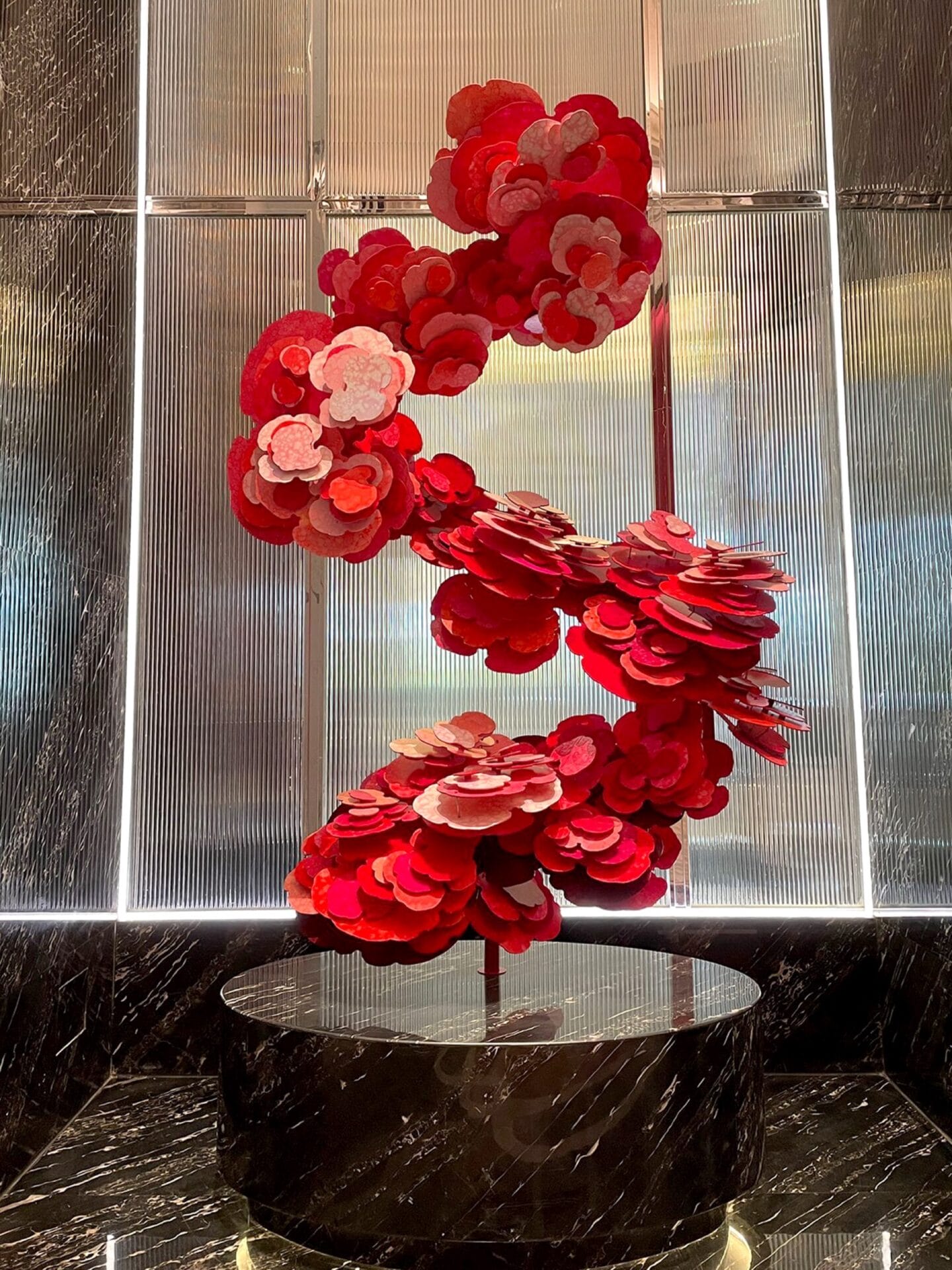 a sculpture made of red, petal-like shapes undulating from a marble plinth in an S-shape