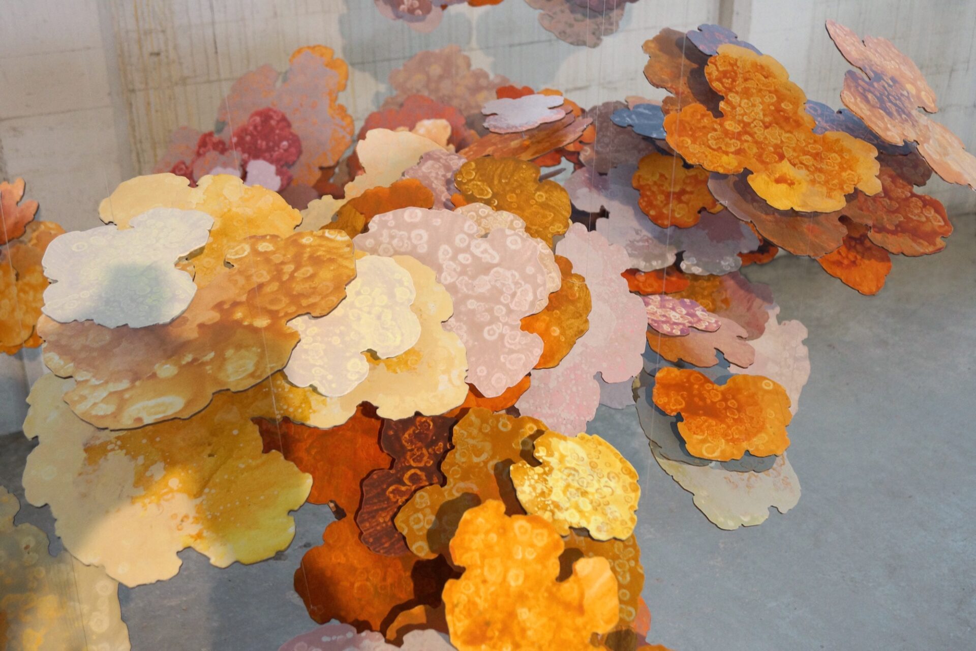 a detail of petal-like shapes painted with oranges, yellows, and pinks, part of a large sculpture consisting of many of the shapes suspended from the ceiling