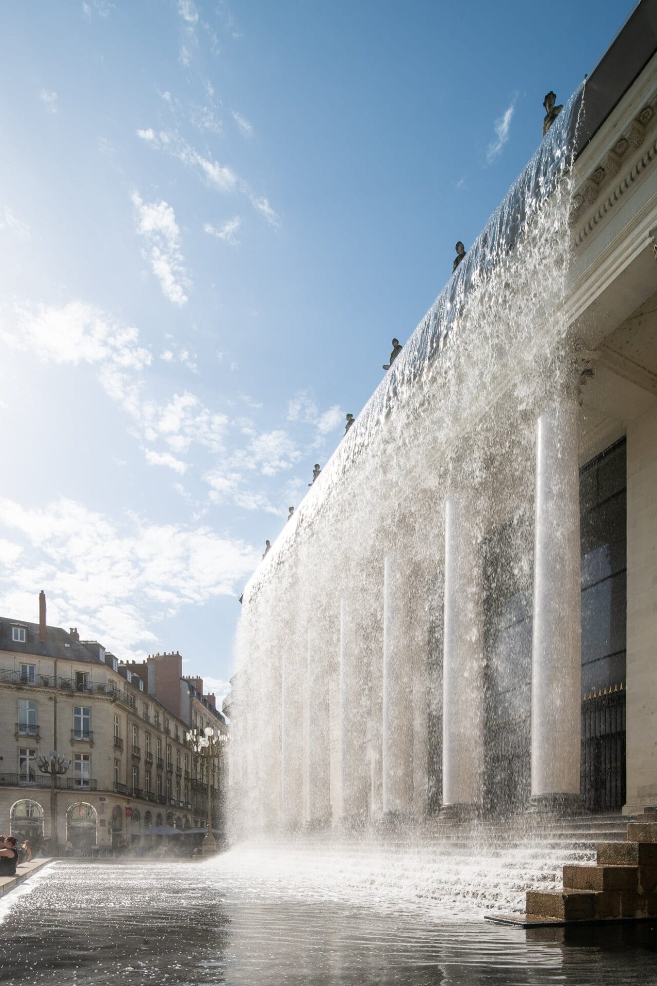 water rains down from a classical style building with columns out front