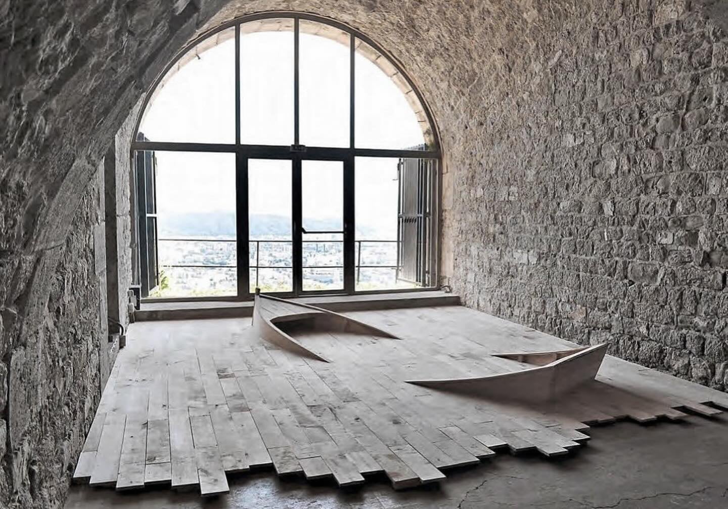 the edges of a small boat emerge from a wooden floor installation in a brick cavern