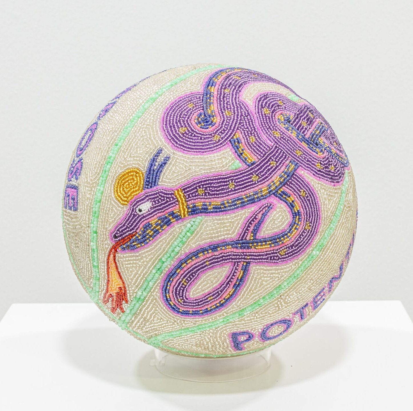 a glass bead-coated spherical sculpture made from a basketball depicting a medieval-style snake on a light green background