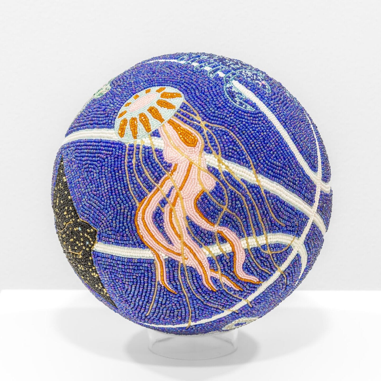 a glass bead-coated spherical sculpture made from a basketball depicting a jellyfish on a dark blue background
