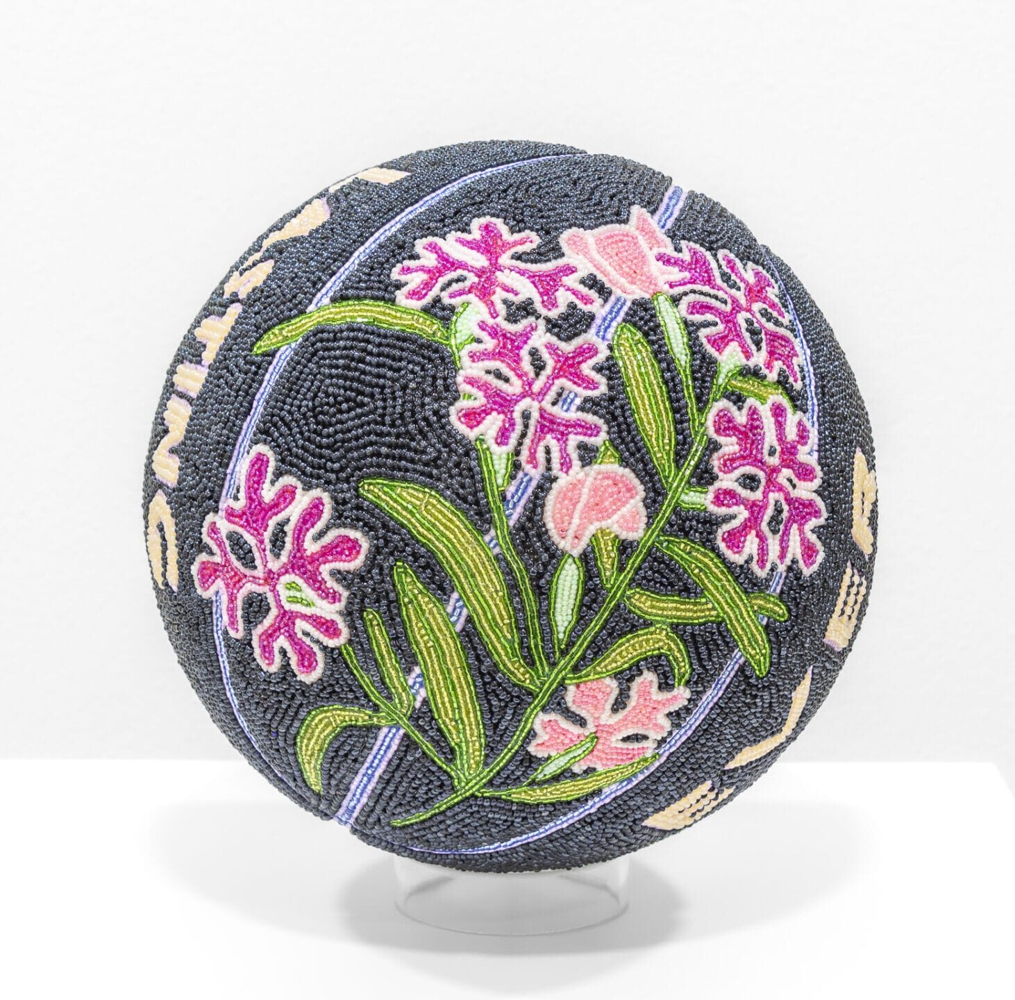 a glass bead-coated spherical sculpture made from a basketball depicting magenta flowers and green leaves on a black background
