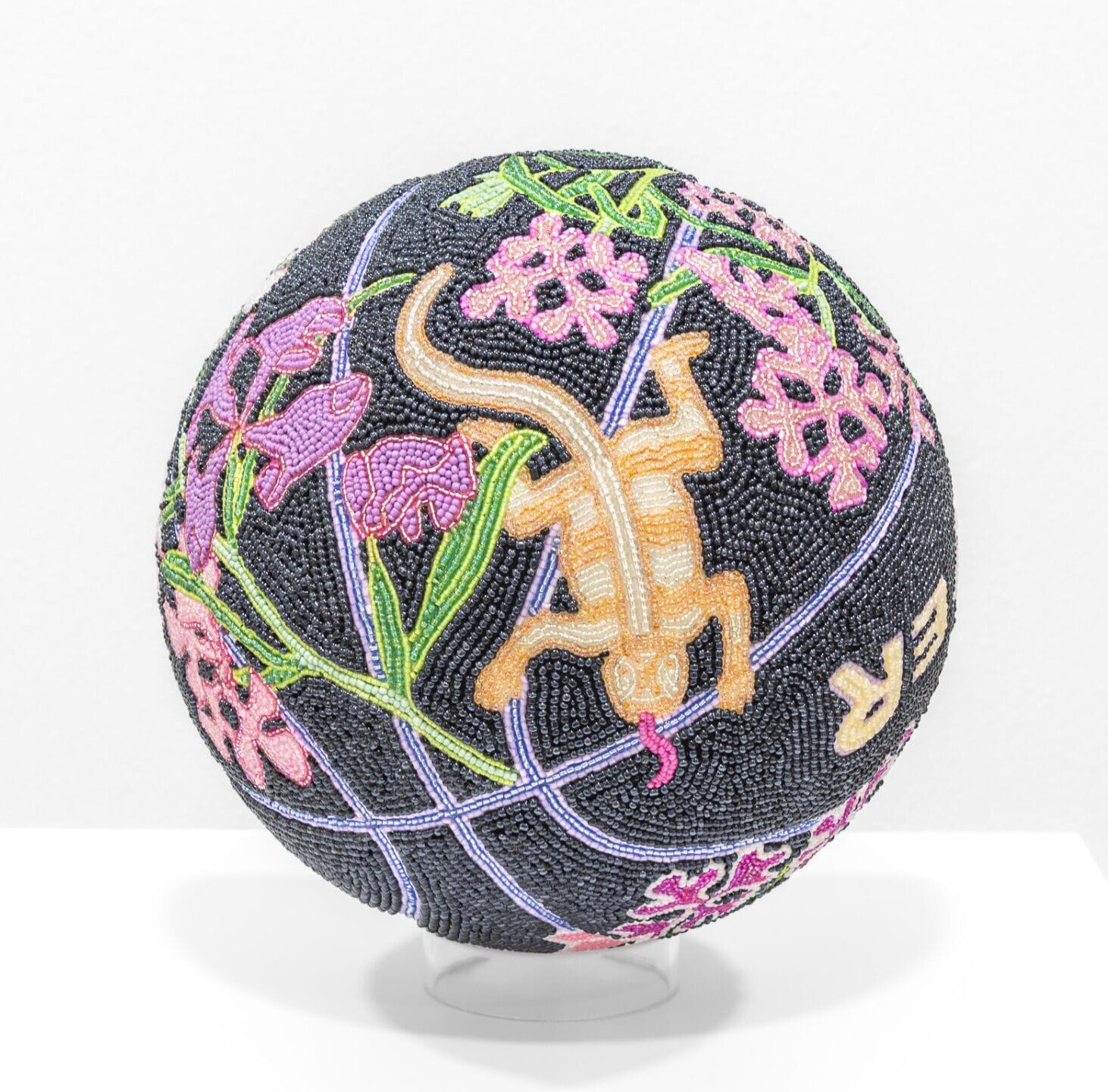 a glass bead-coated spherical sculpture made from a basketball depicting a lizard an flowers on a black backround