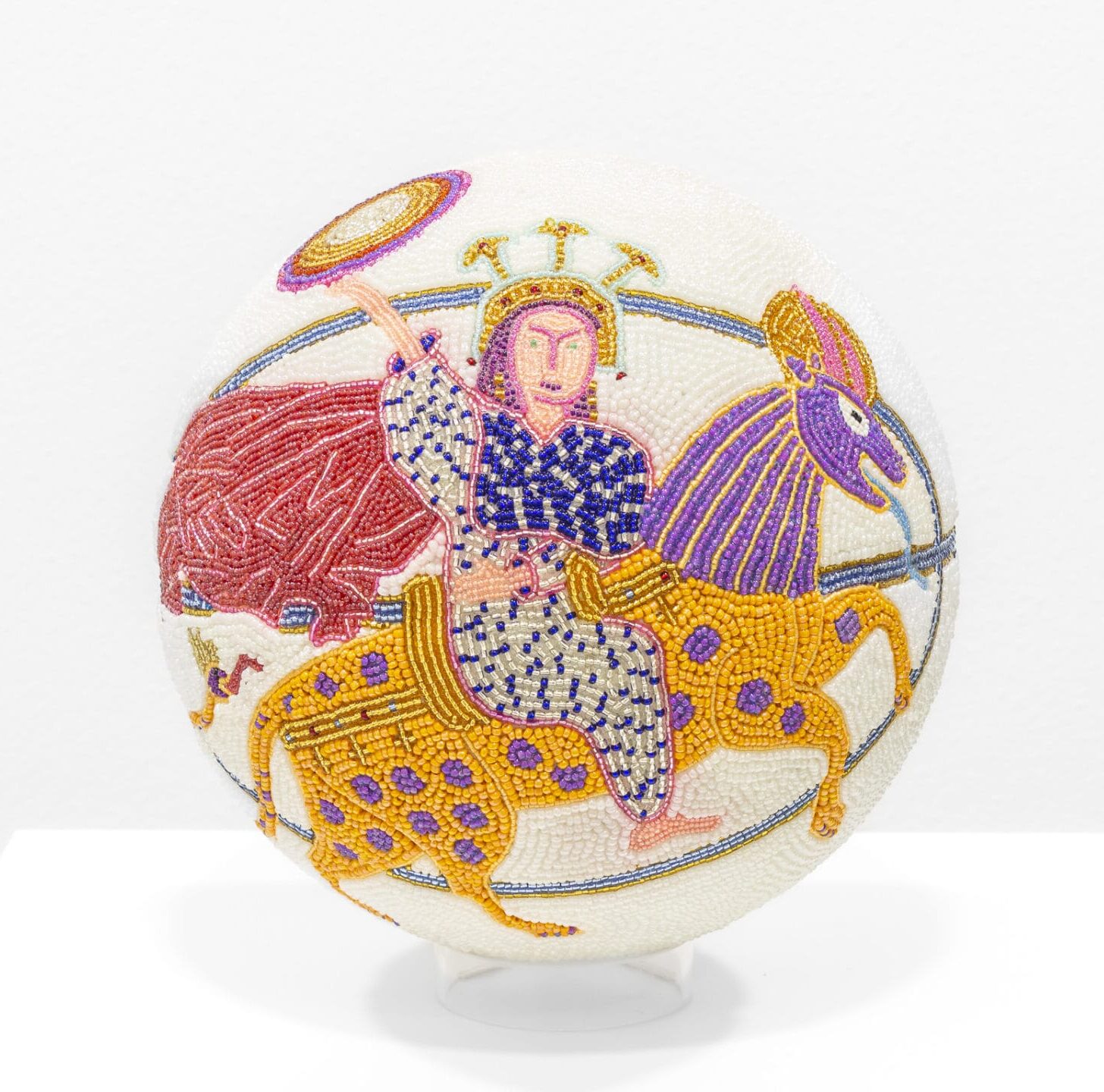 a glass bead-coated spherical sculpture made from a basketball depicting a woman on horseback, wearing a crown, on a white background
