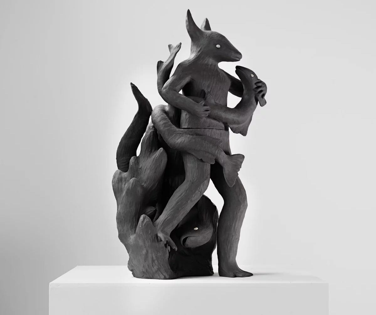 a black ceramic sculpture of fish winding around a human-animal hybrid