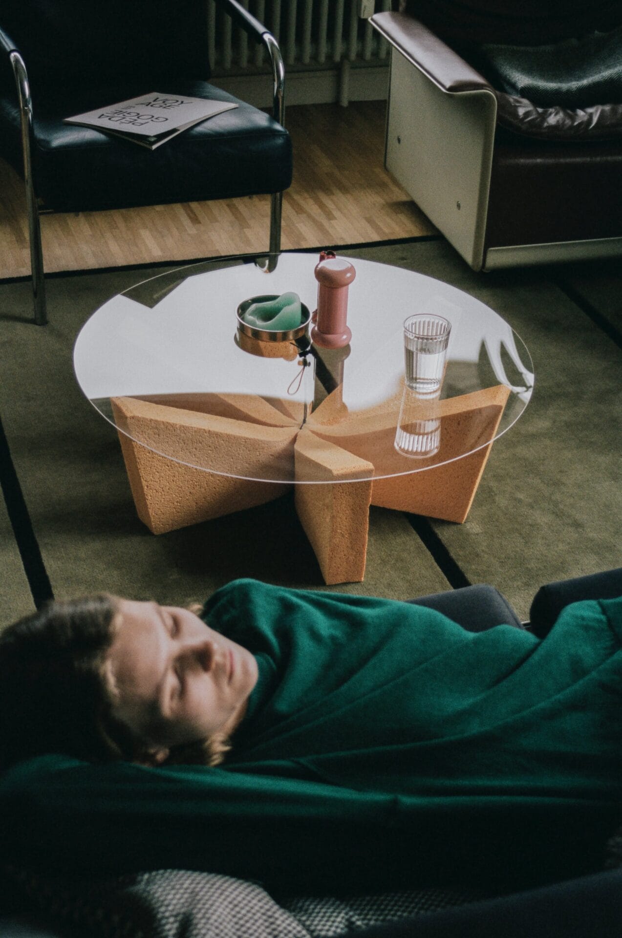 an acrylic top with a glass of water and other objects sits atop a sponge base while a person sleeps on a couch nearby