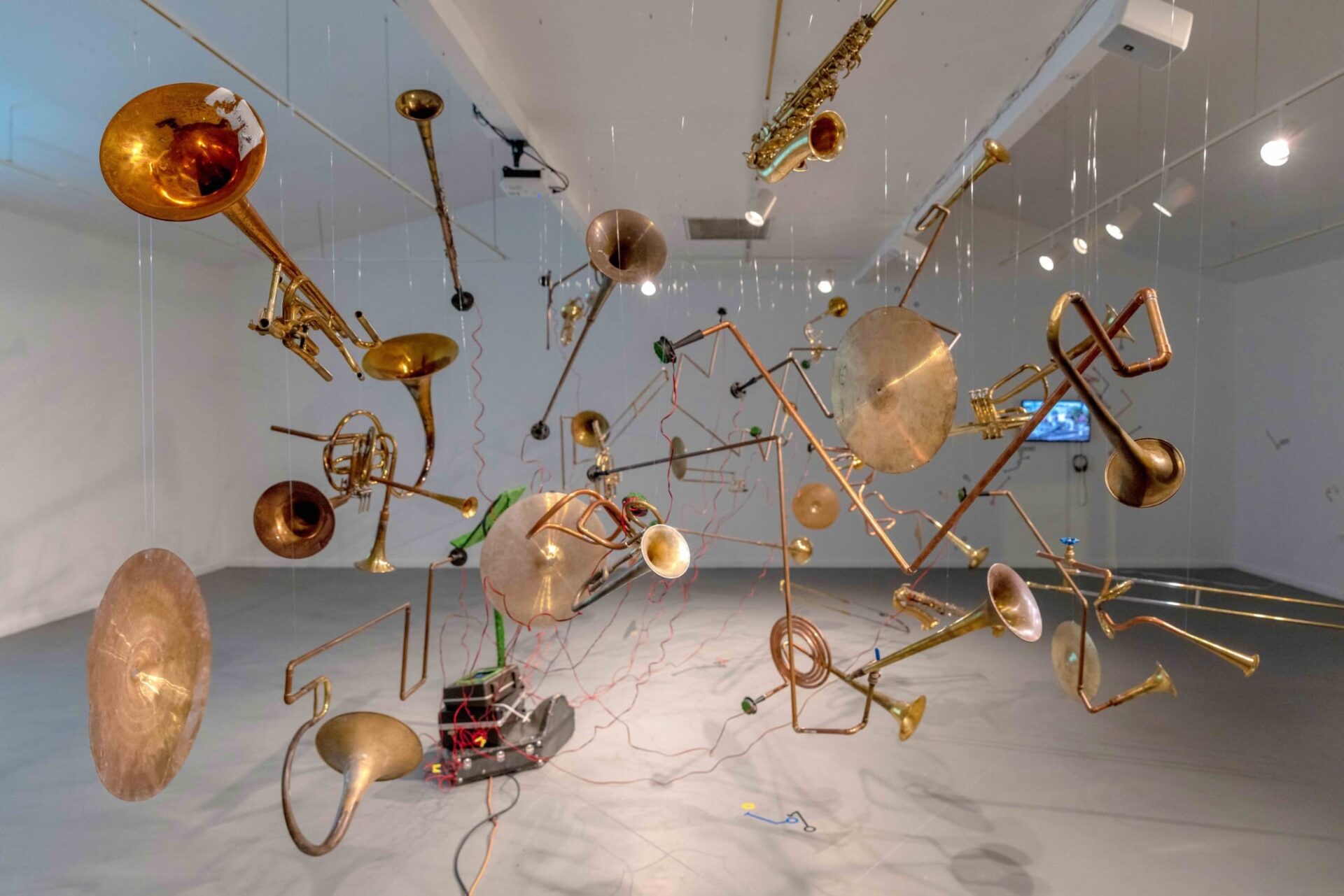 a cluster of suspended brass instruments hang in a gallery