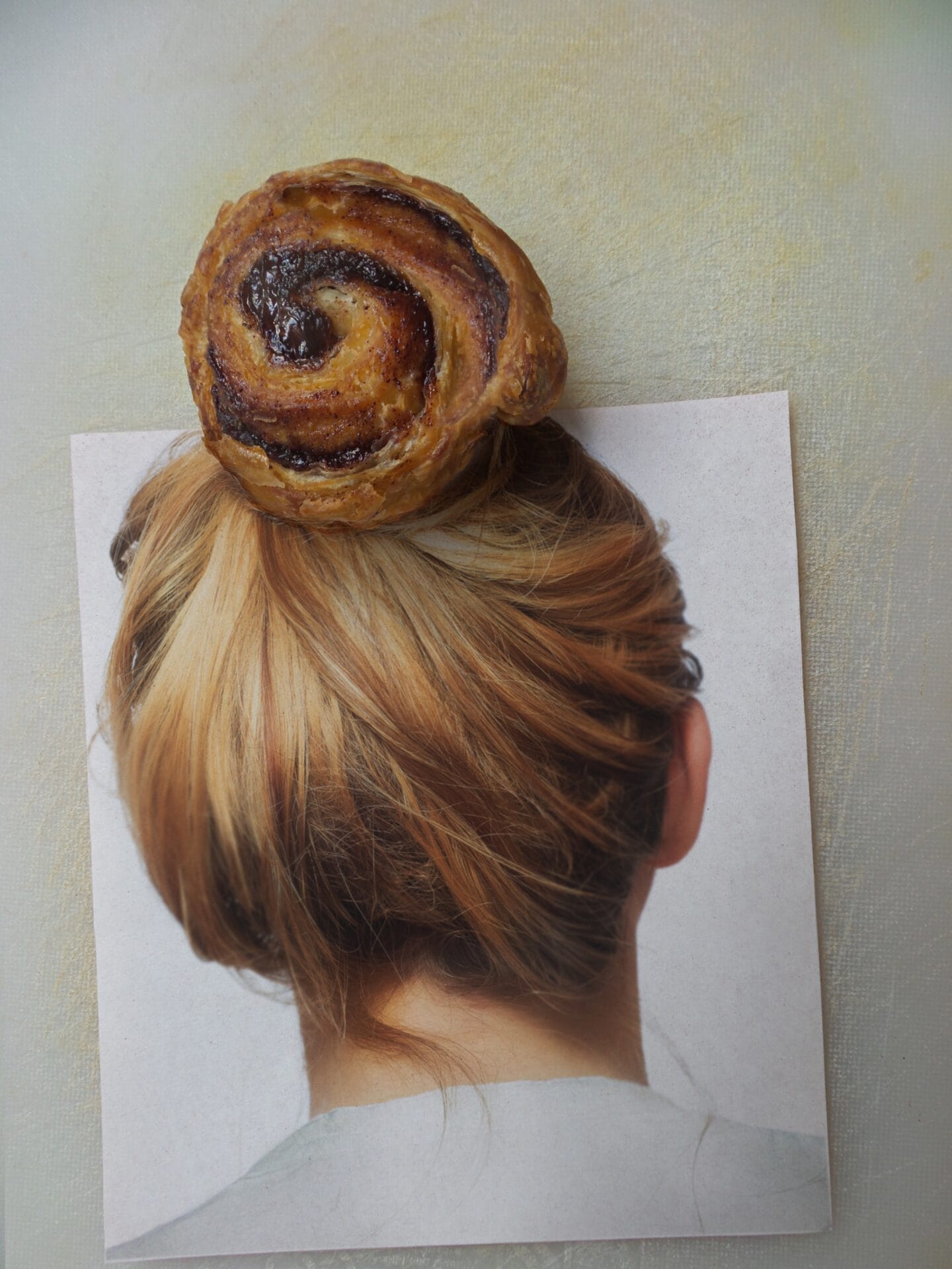 a photograph of a woman with her hair tied up in a bun, and a cinnamon bun situated where her own hair bun would be