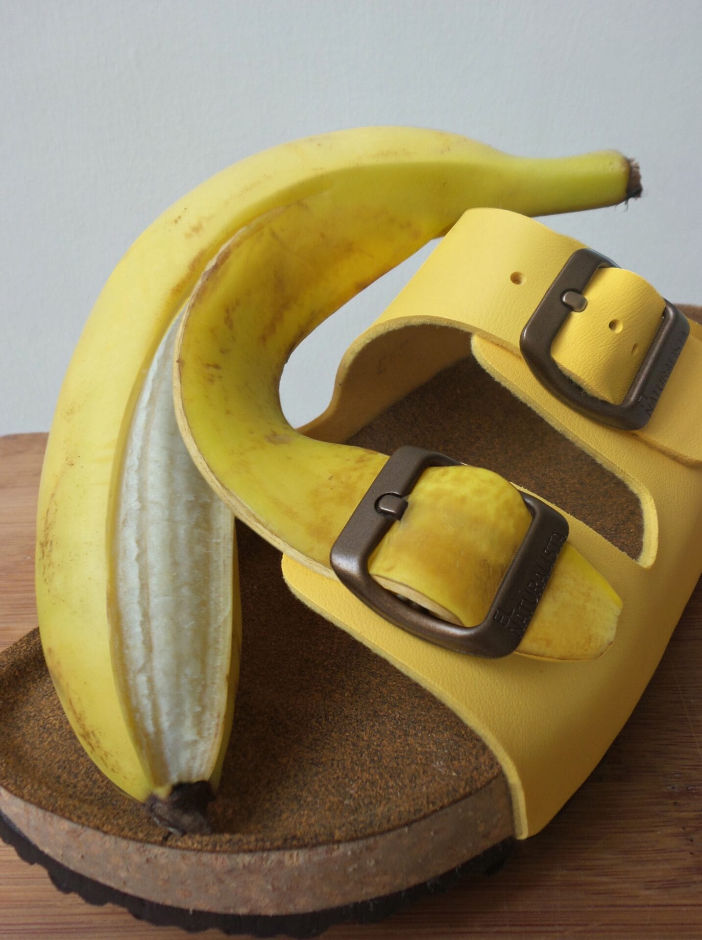 a yellow Birkenstock sandal with a banana peel strapped through one of the buckles
