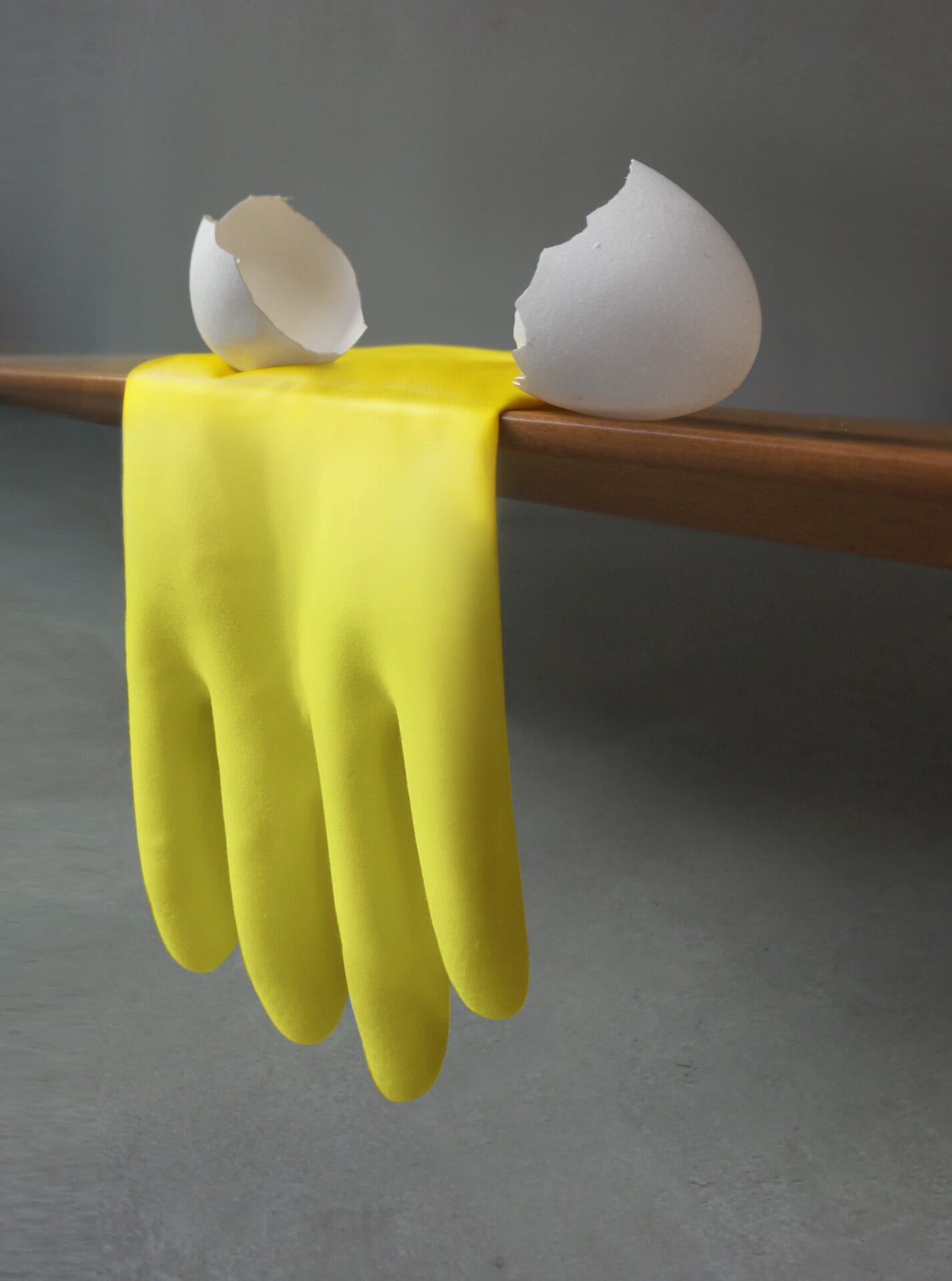 a yellow rubber glove drapes off of a shelf, with a broken egg shell near it, resembling the liquid part of the egg dripping