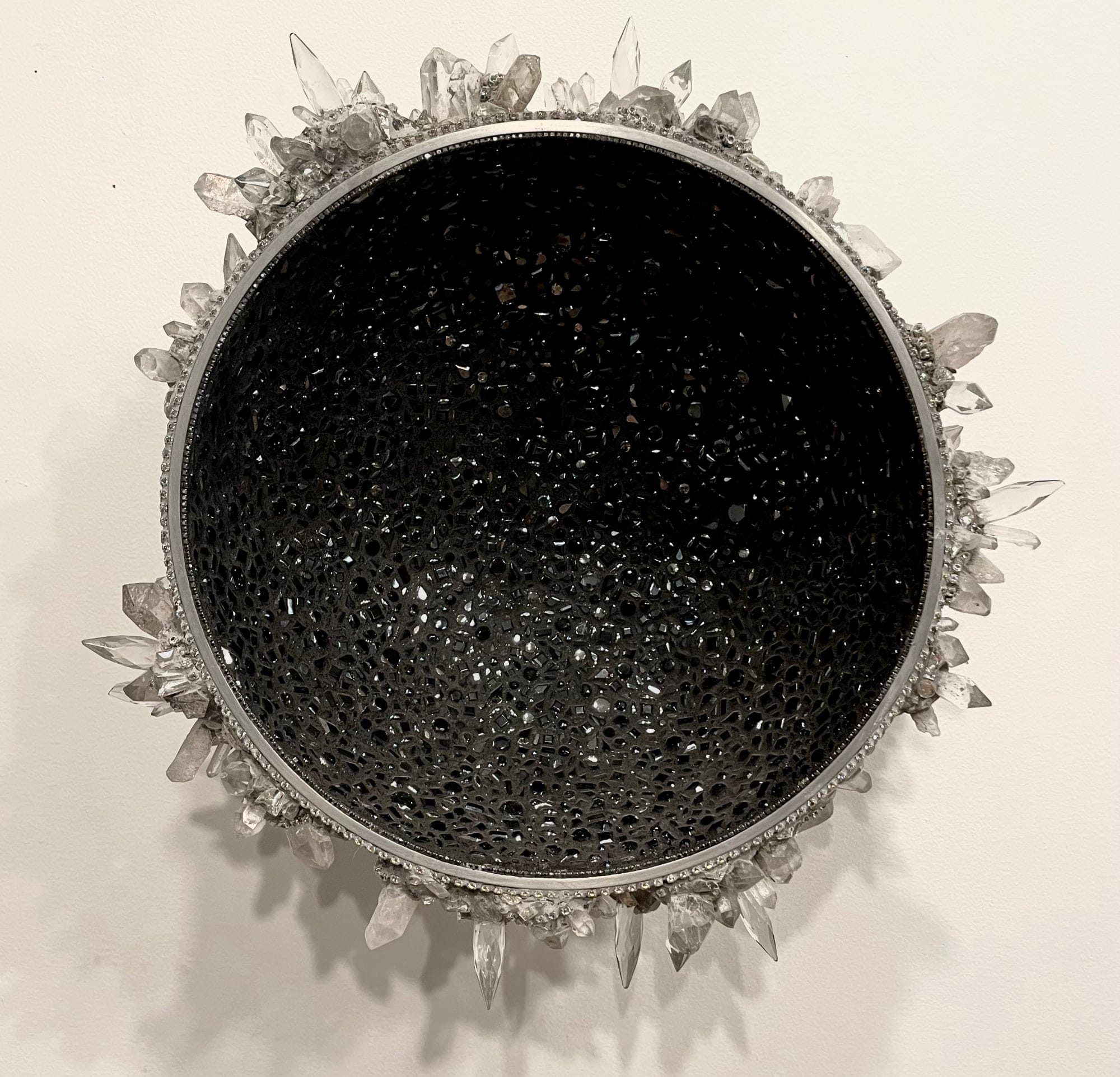 a half-orb sculpture with a glimmering black inside and sharp clear crystals around the outside