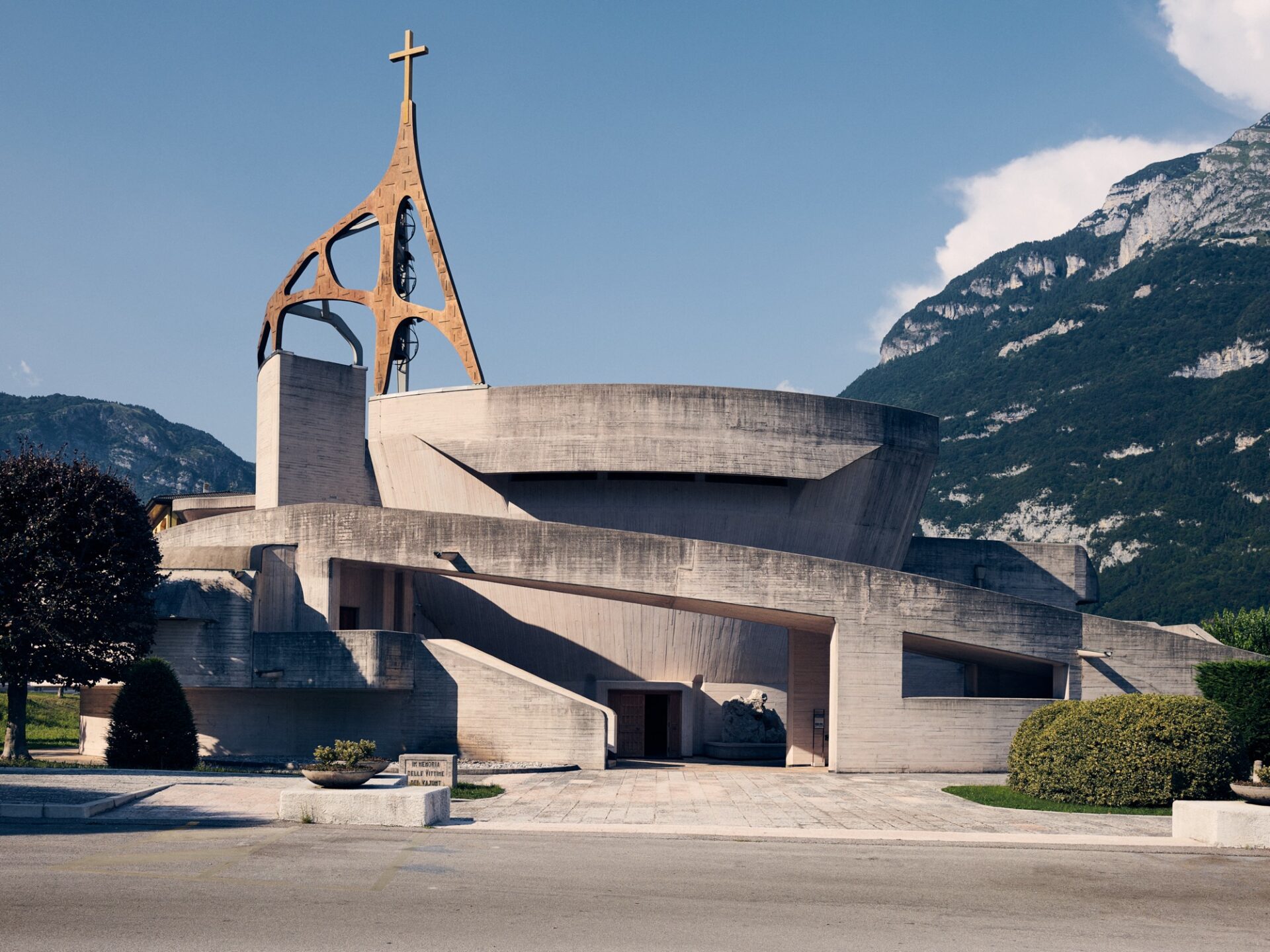 the exterior of a concrete brutalist church in Italy, set against the mountains