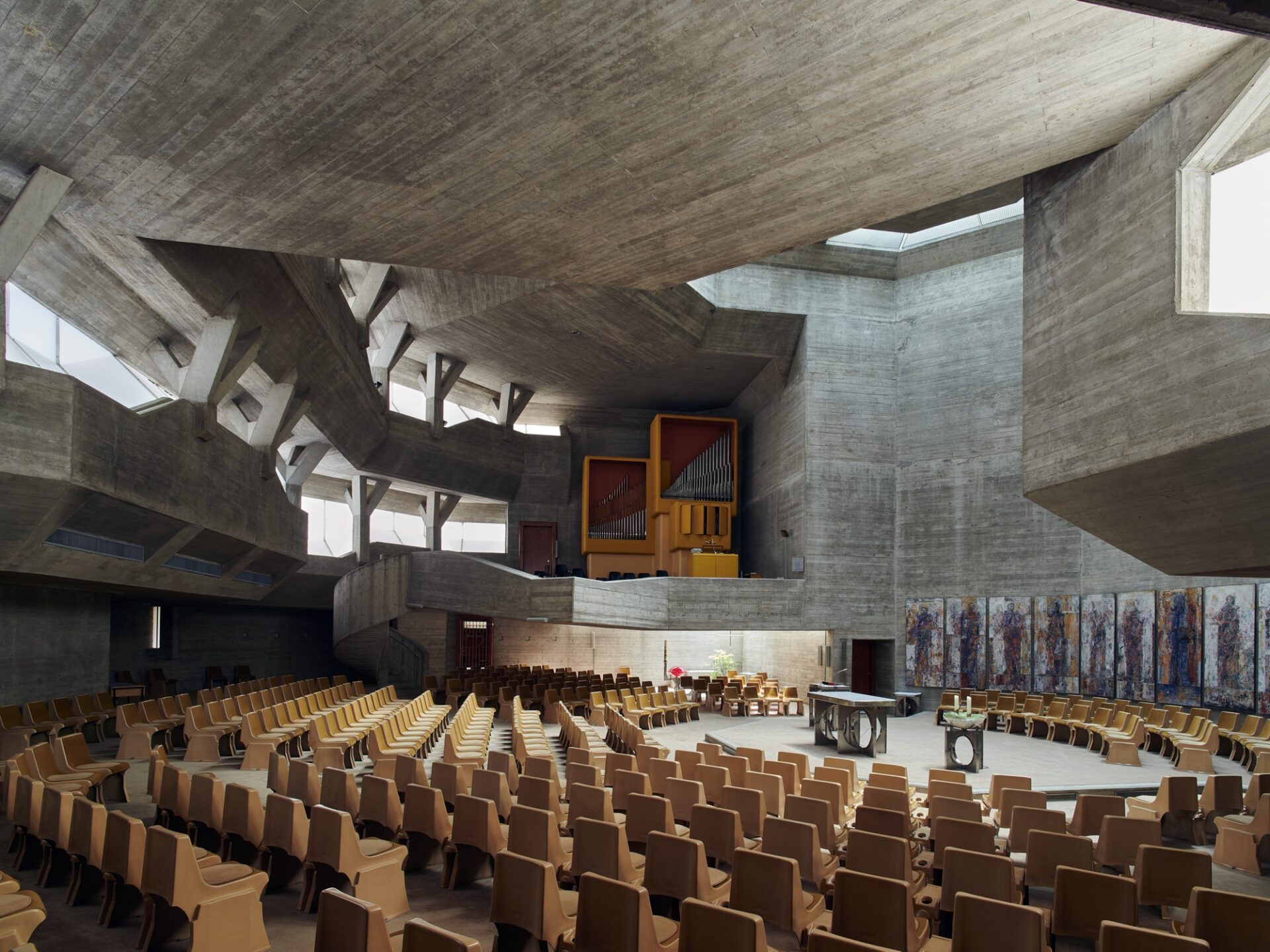 an interior overview of a large brutalist church with angular concrete walls and wooden seats