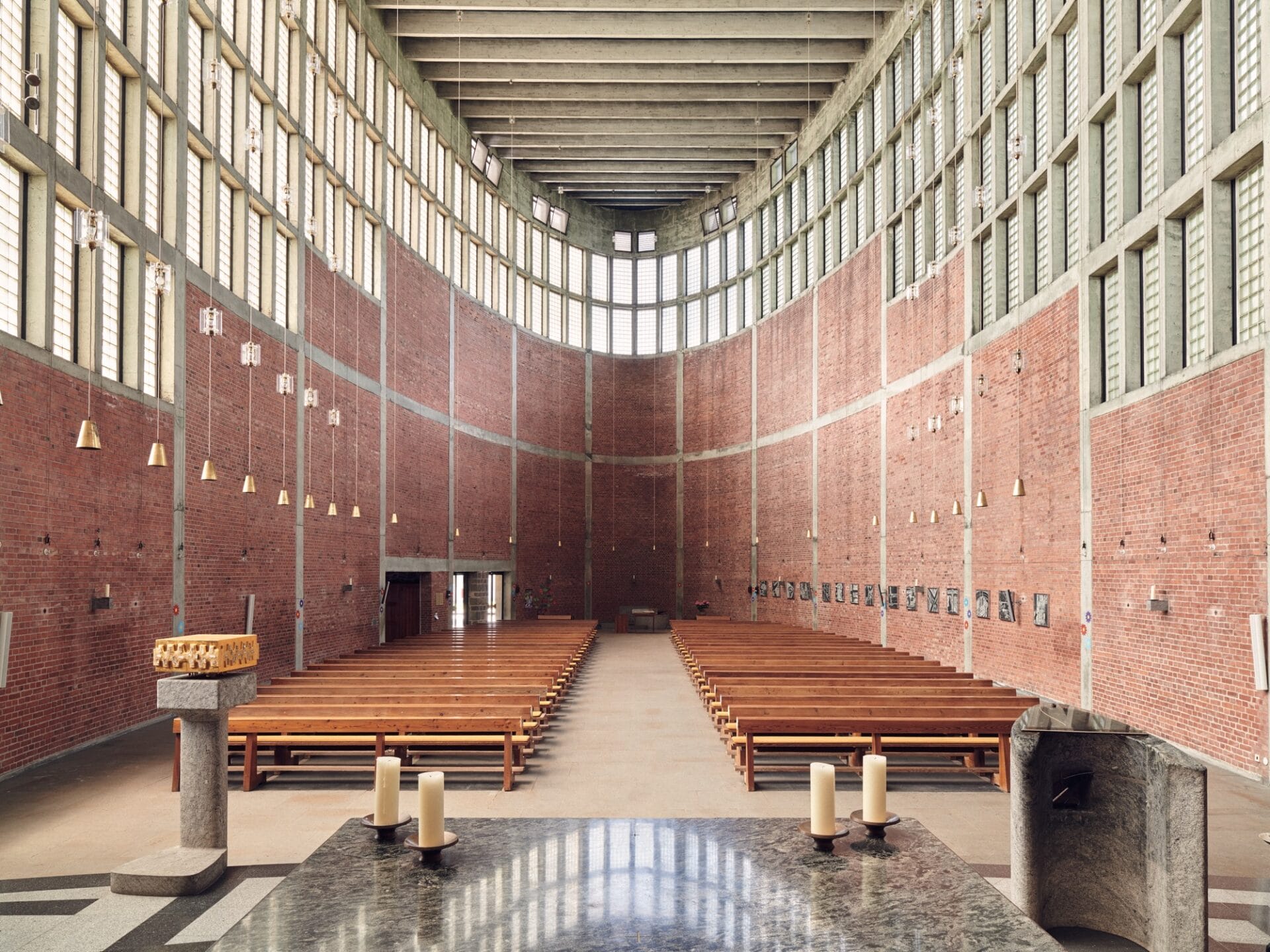 an interior overview of a large brutalist church with curved brick and concrete walls and wooden pews