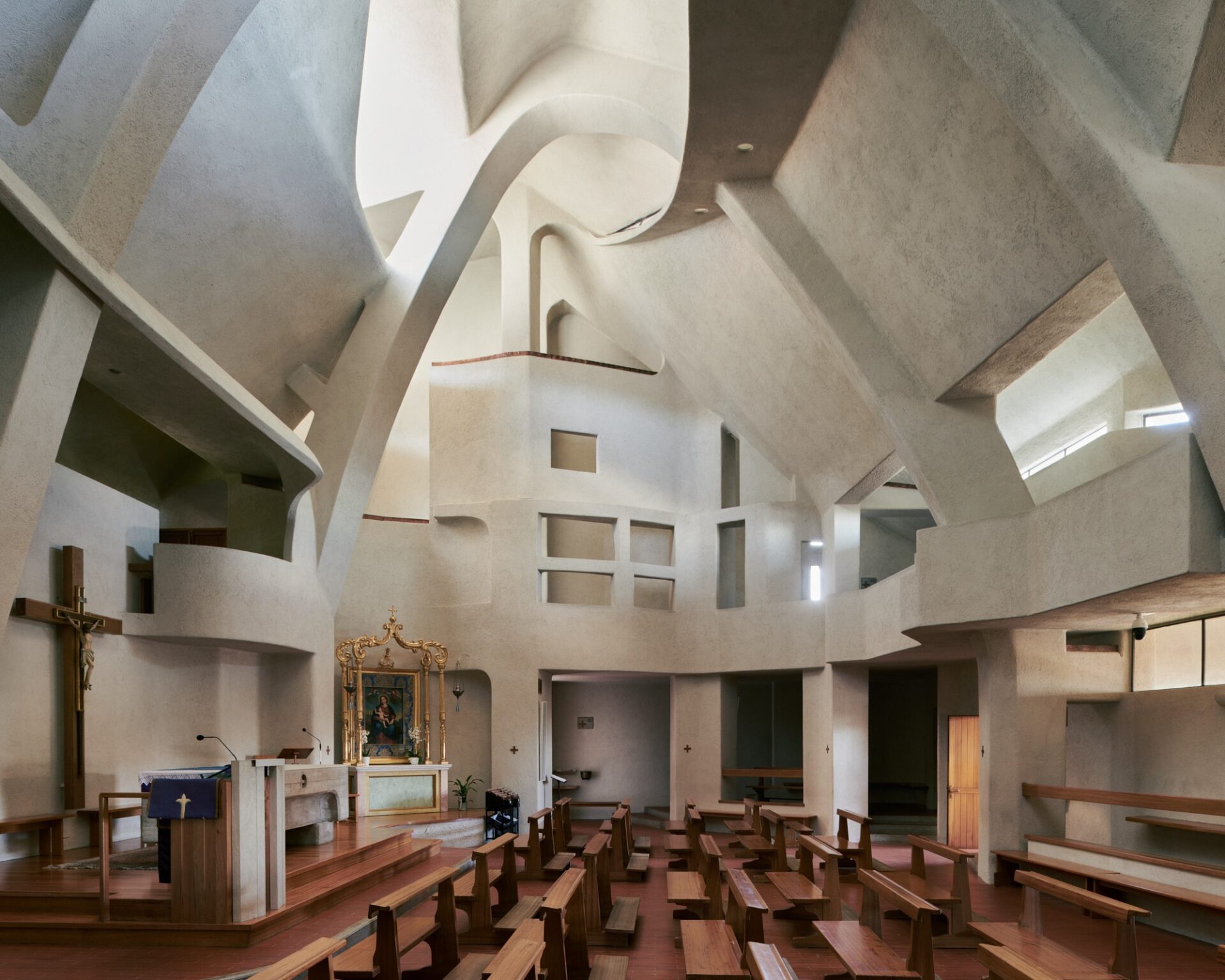 an interior overview of a large brutalist church with angular concrete walls and wooden pews