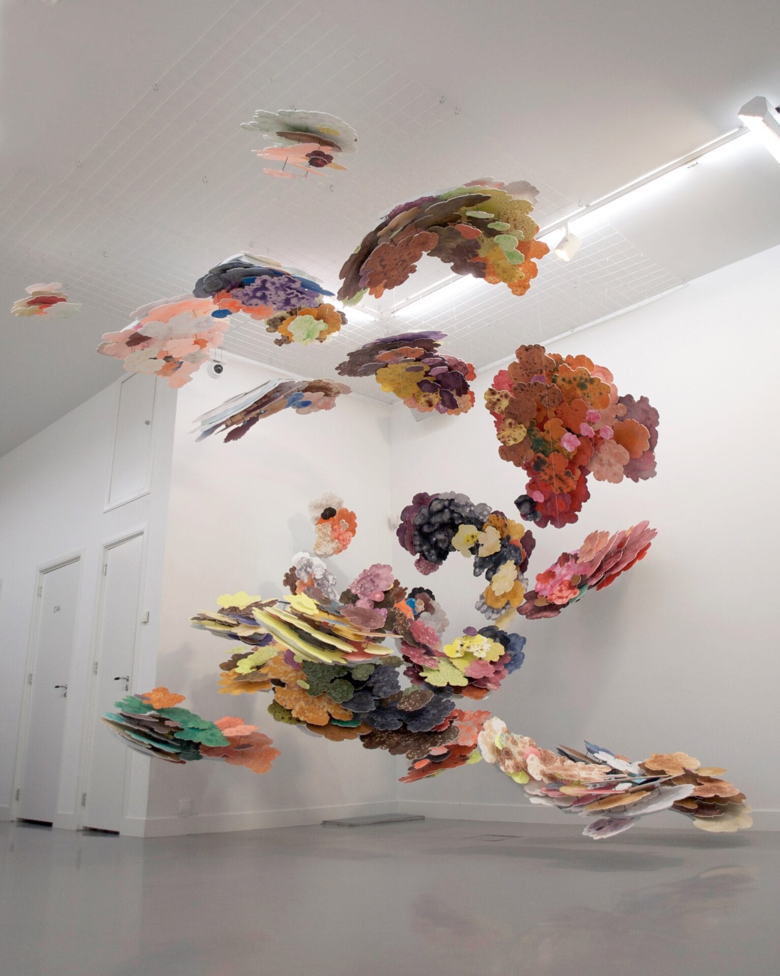 a suspended installation in a white space made of numerous petal-shaped panels in different colors that cluster together and look as though they are falling from the ceiling
