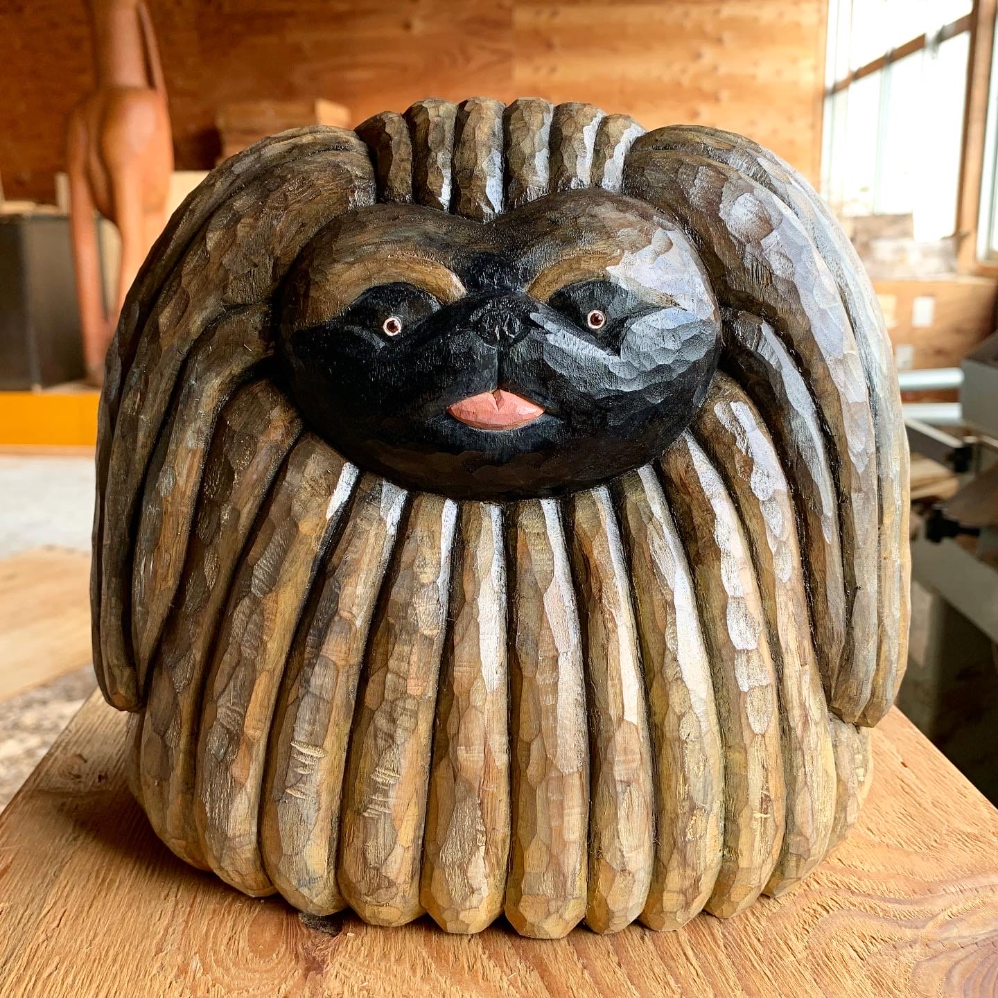 a carved wooden sculpture of a Shih Tzu in a woodworking studio