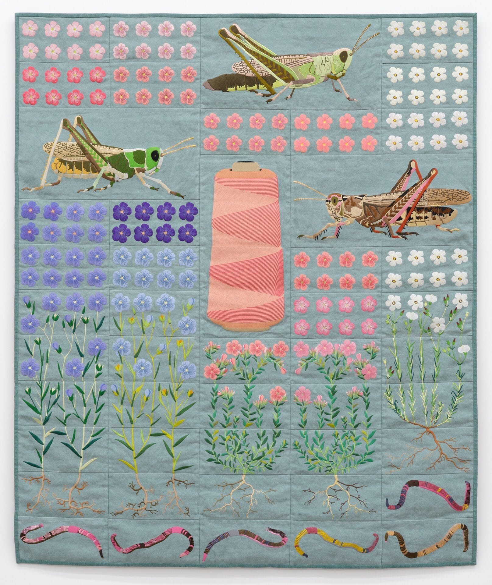a quilt with patterns of flowers, grasshoppers, plants, a spool of thread, and worms on a light blue background