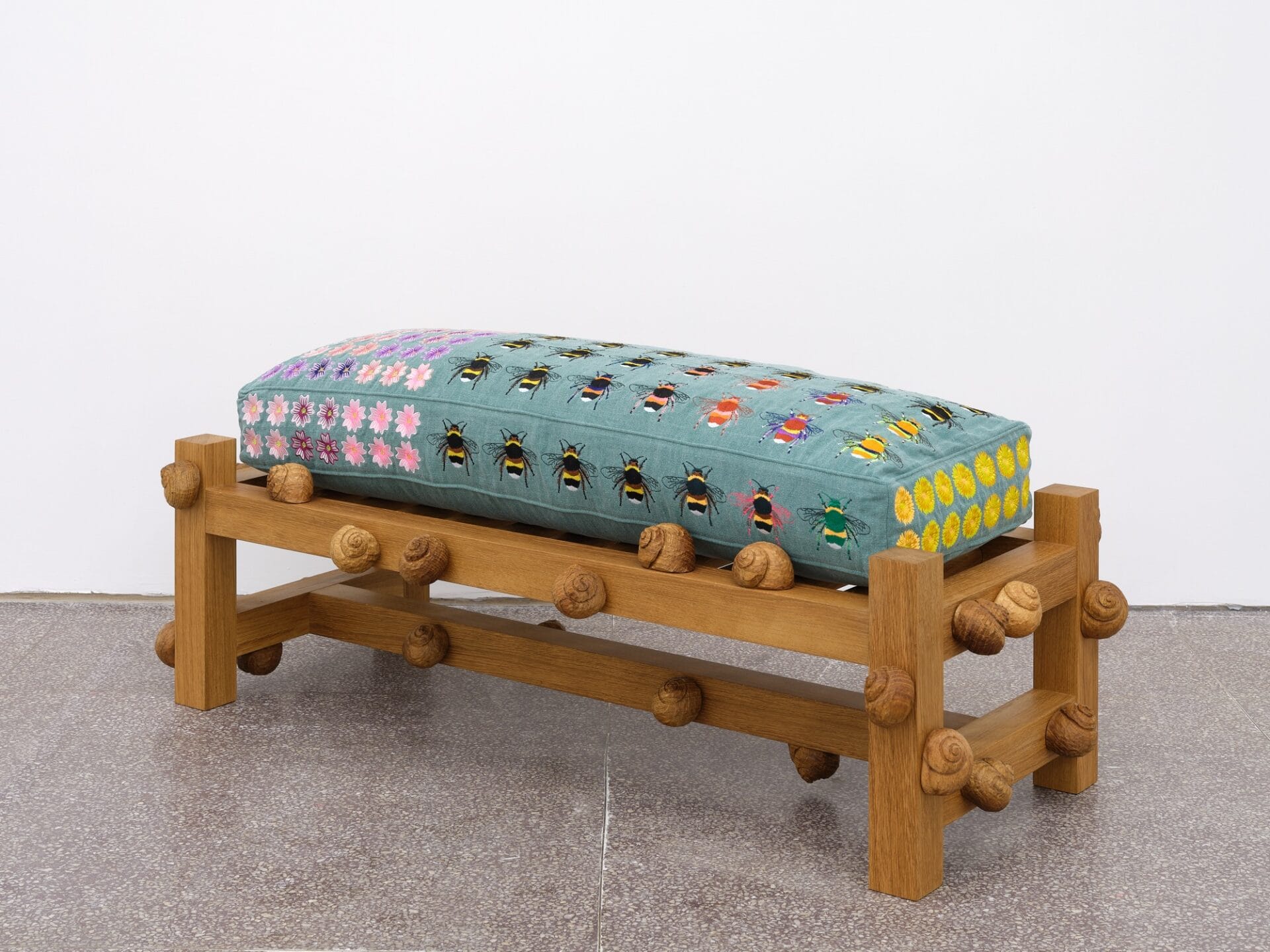 an oak bench carved with snail shells with a quilted cushion containing patterns of bugs and flowers