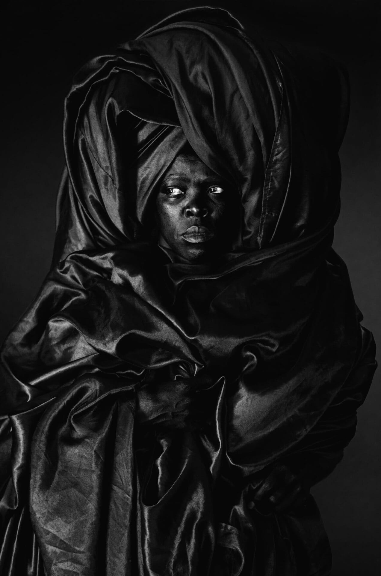 a black and white image of the artist wrapped in a swath of fabric