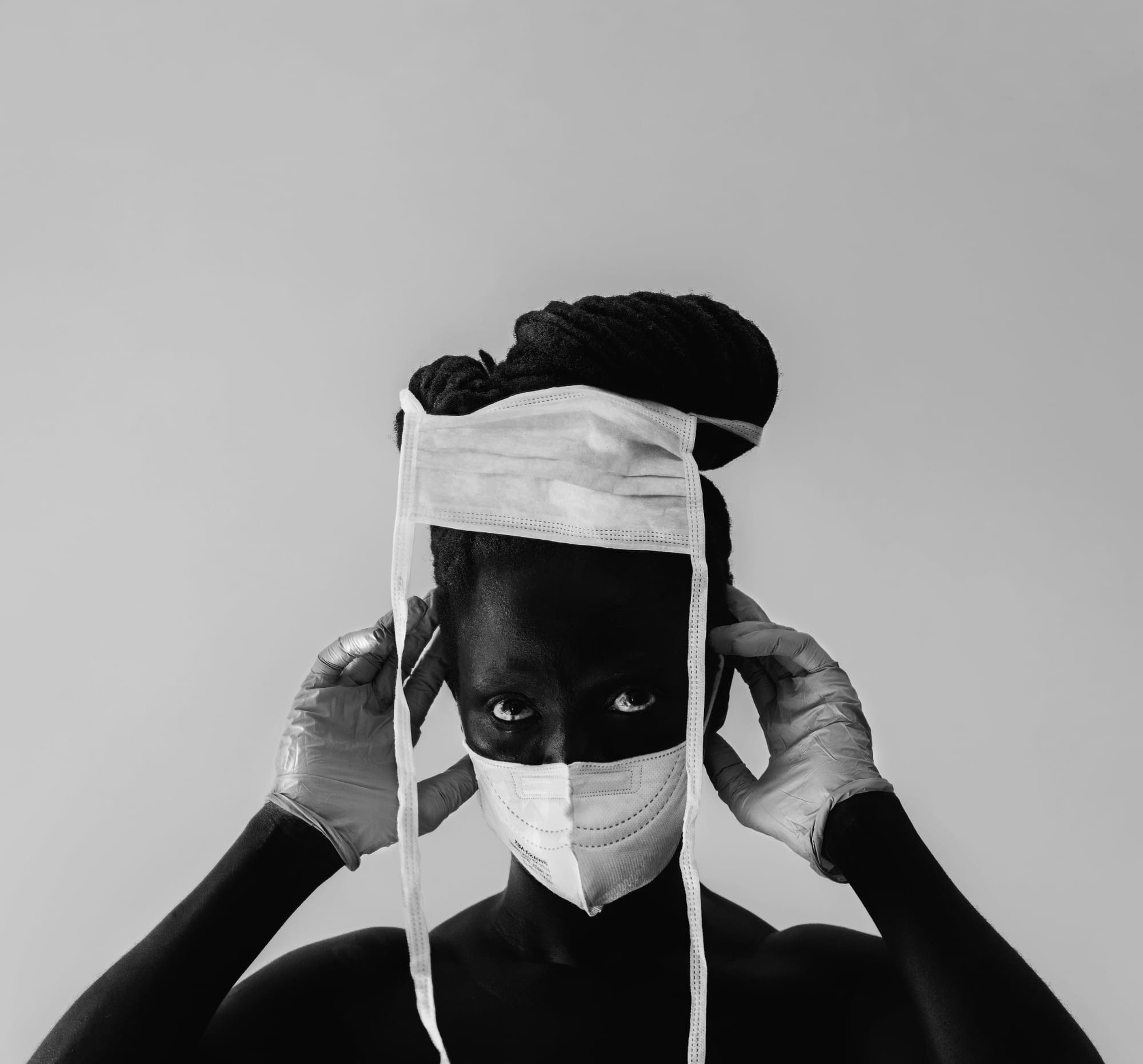a black and white portrait of the artist wearing two white masks on their face and head and gloves