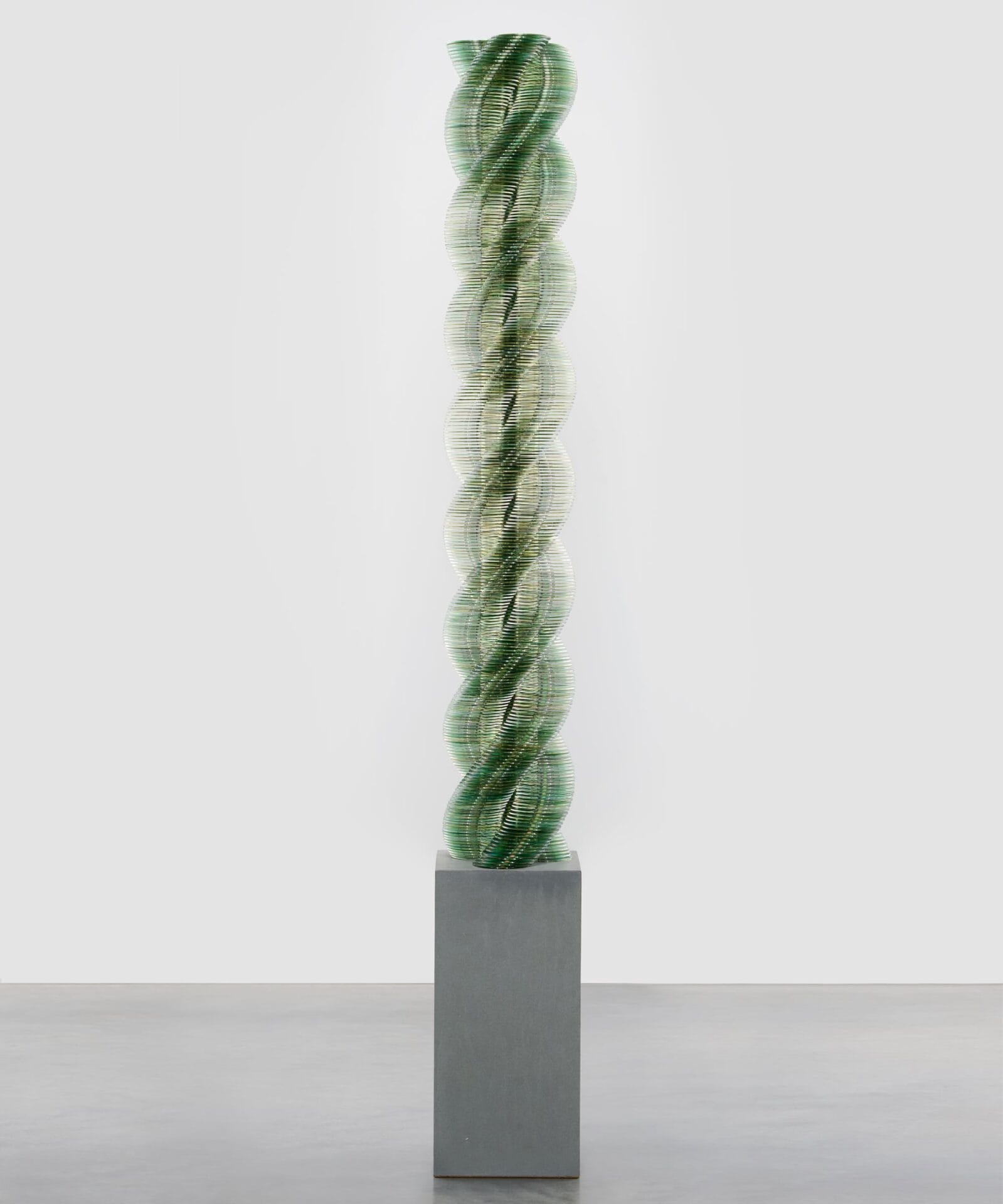 a twisting green sculpture on a concrete pedestal