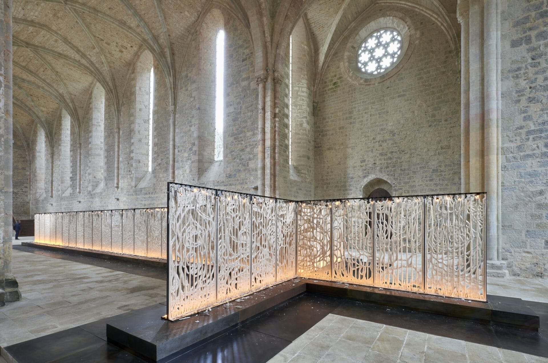 a large cross shaped installation with panels of wax stands in an ornate brick hall