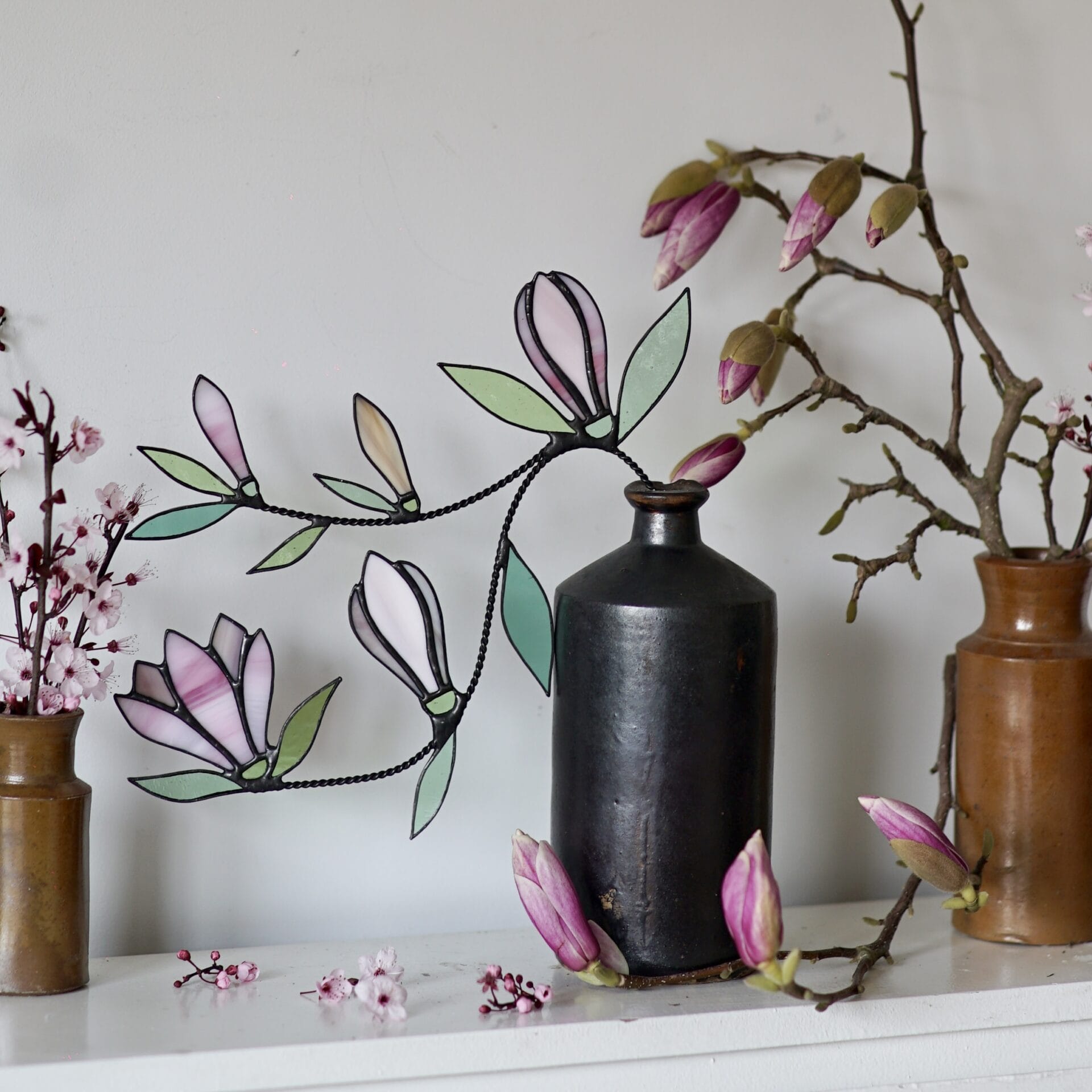 stained glass magnolia flowers and vines in ceramic vases alongside live specimens