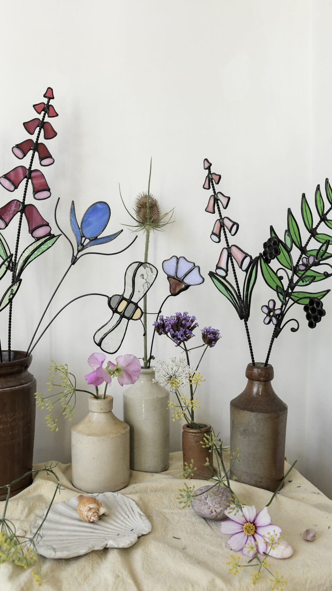 stained glass flowers and vines in ceramic vases alongside live specimens
