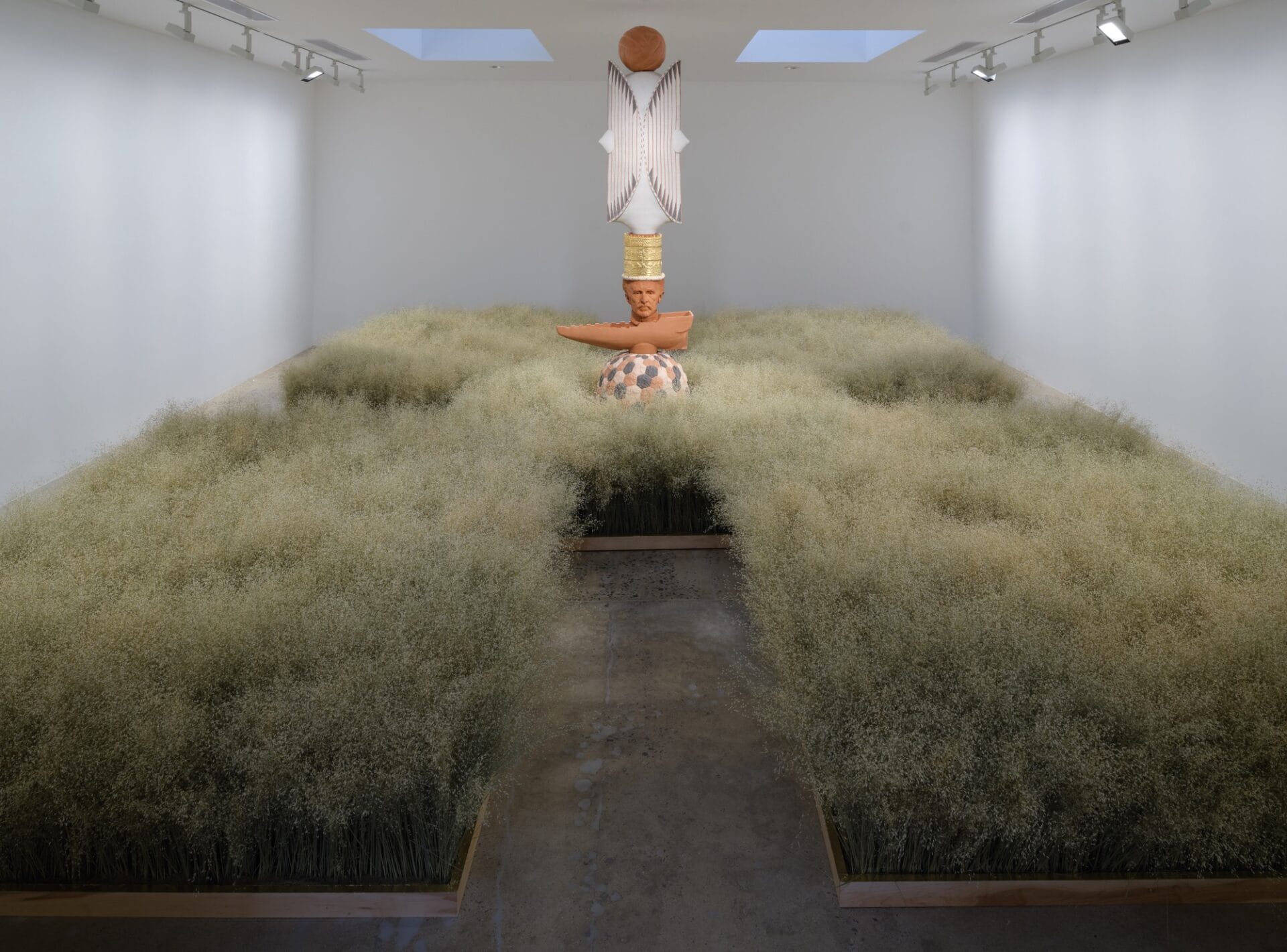 a large-scale installation in a gallery space with a rice field installation that viewers can walk through on a pathway, leading to a single, totem-like sculpture