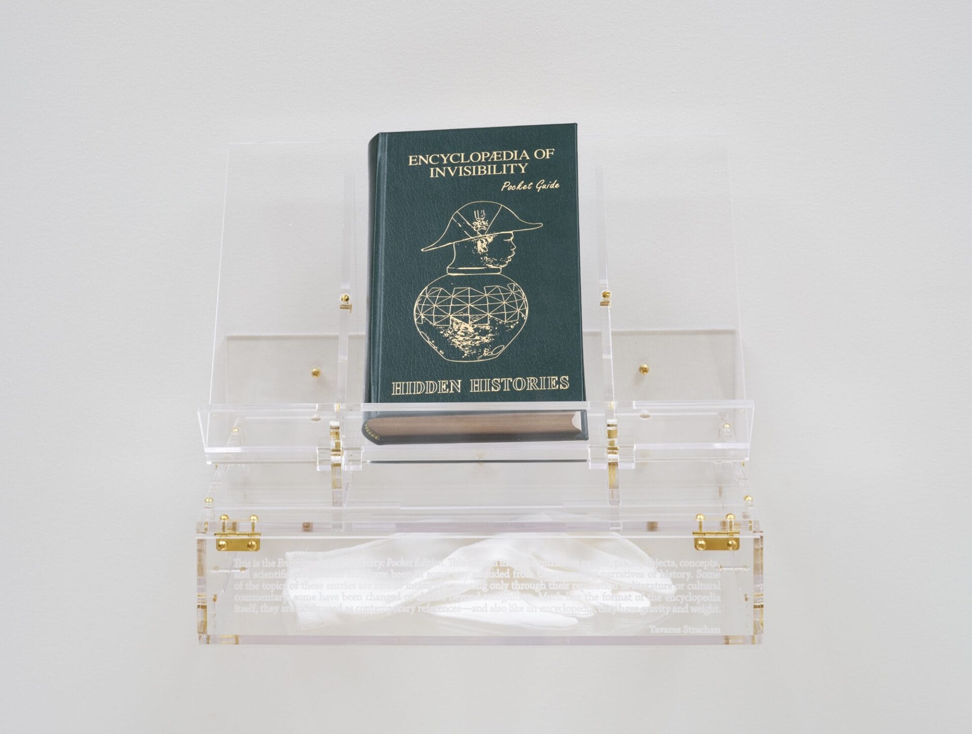 a sculpture of a pocket-size book called the Encyclopedia of Invisibility: Hidden Histories, displayed on an acrylic stand with white gloves inside