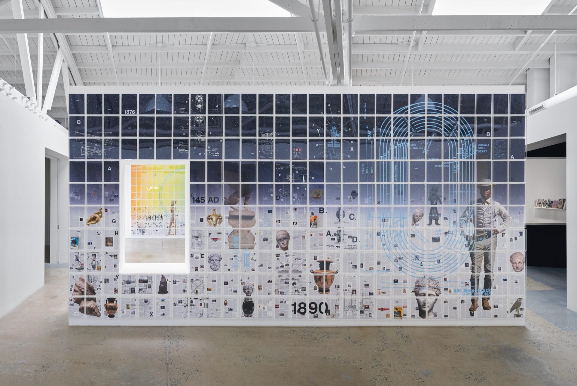 a large installation in a gallery space showing a wall with a window through it to another installation behind. the wall is covered in a grid of rectangles that reveal a sweeping scene with a figure on the right and numerous vases and other elements