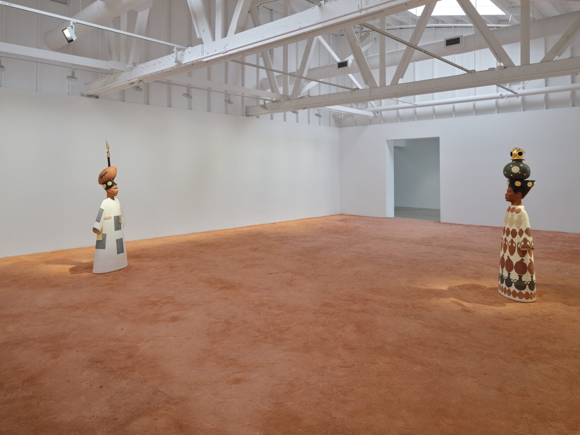 two figurative sculptures depicting explorer Matthew Henson and U.S. Army diver Andrea Crabtree, in a large gallery space with a sandy floor