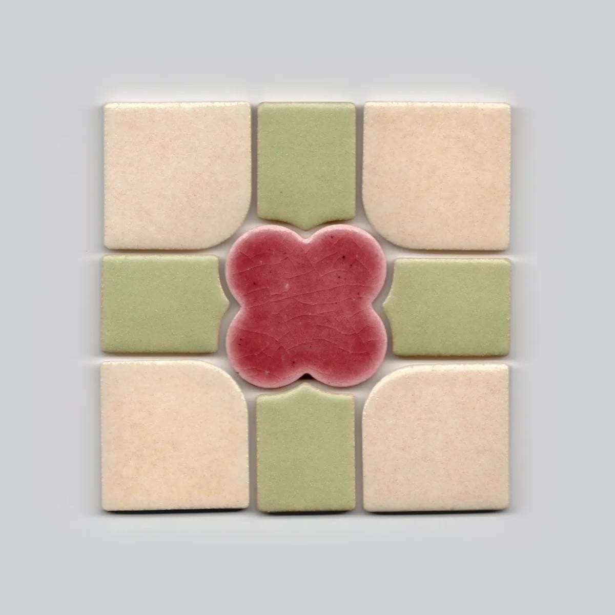 a square tile with a pink flower at the center and green and beige pieces around it