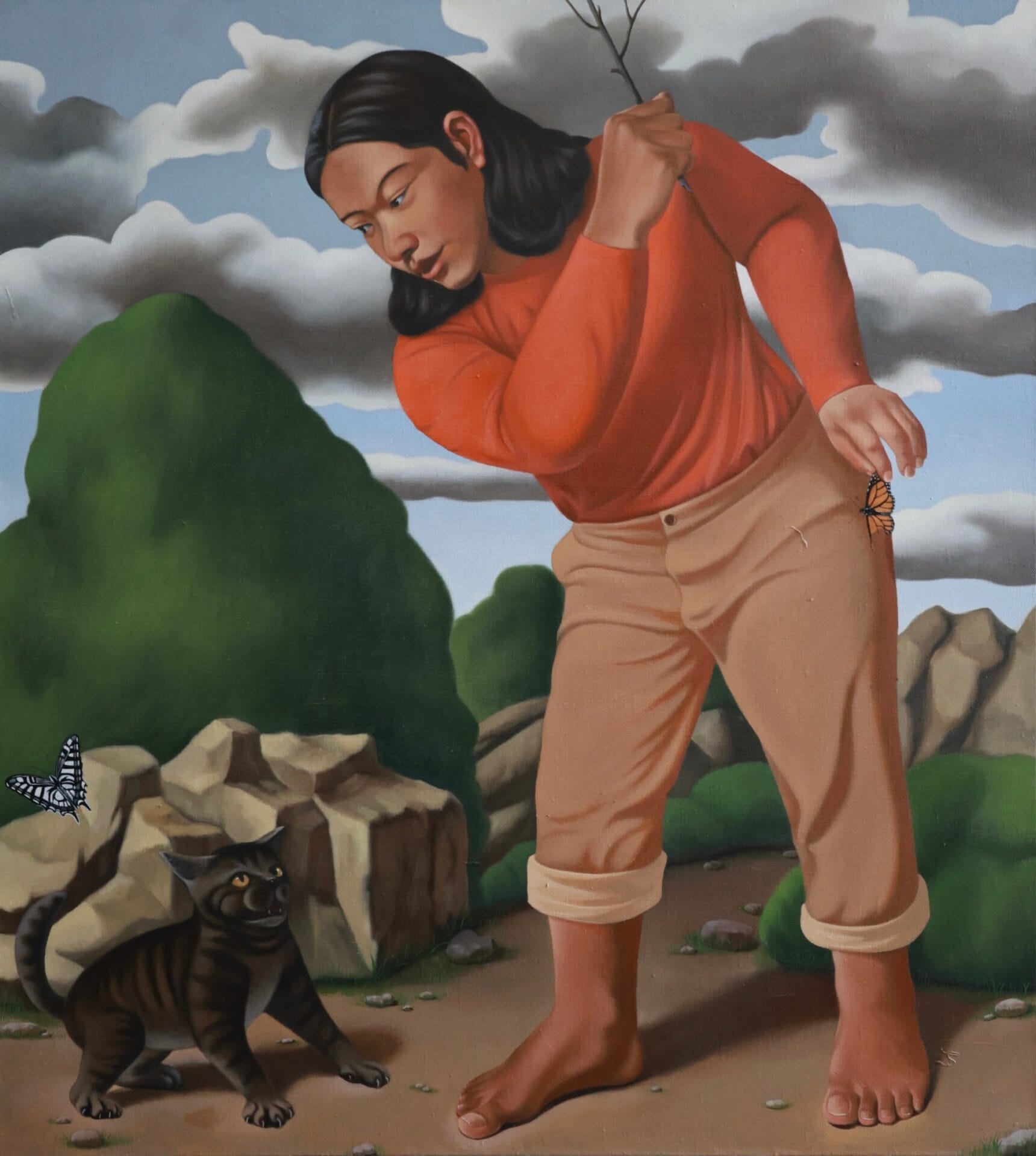 a man with long hair, an orange long-sleeve shirt, and rolled up tan pants grips a twig as if to hit a striped cat near a butterfly