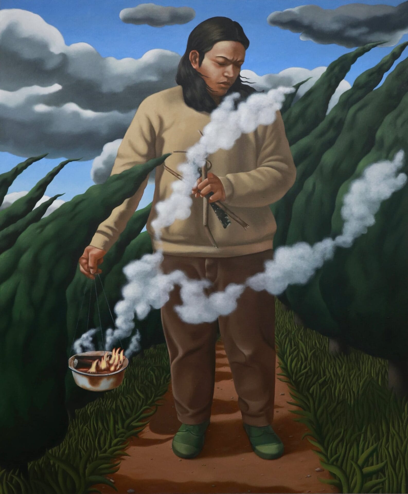 a man in a beige sweatshirt with brown pants walks on a path holding a kettle with fire and smoke
