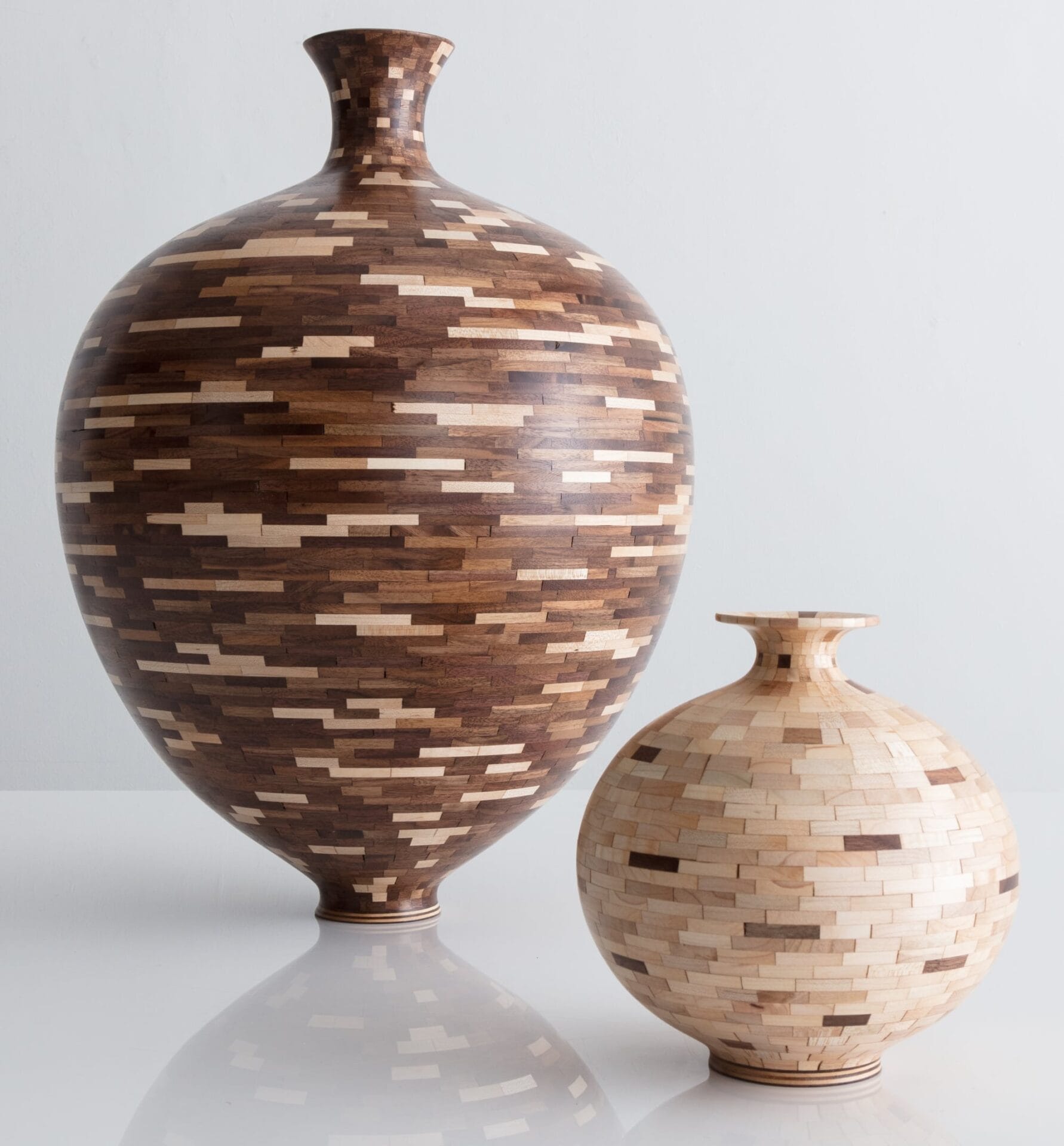 two curvy wooden vessels made of dark and light wood components fitted together, the left is tall and darker and the left is short and lighter
