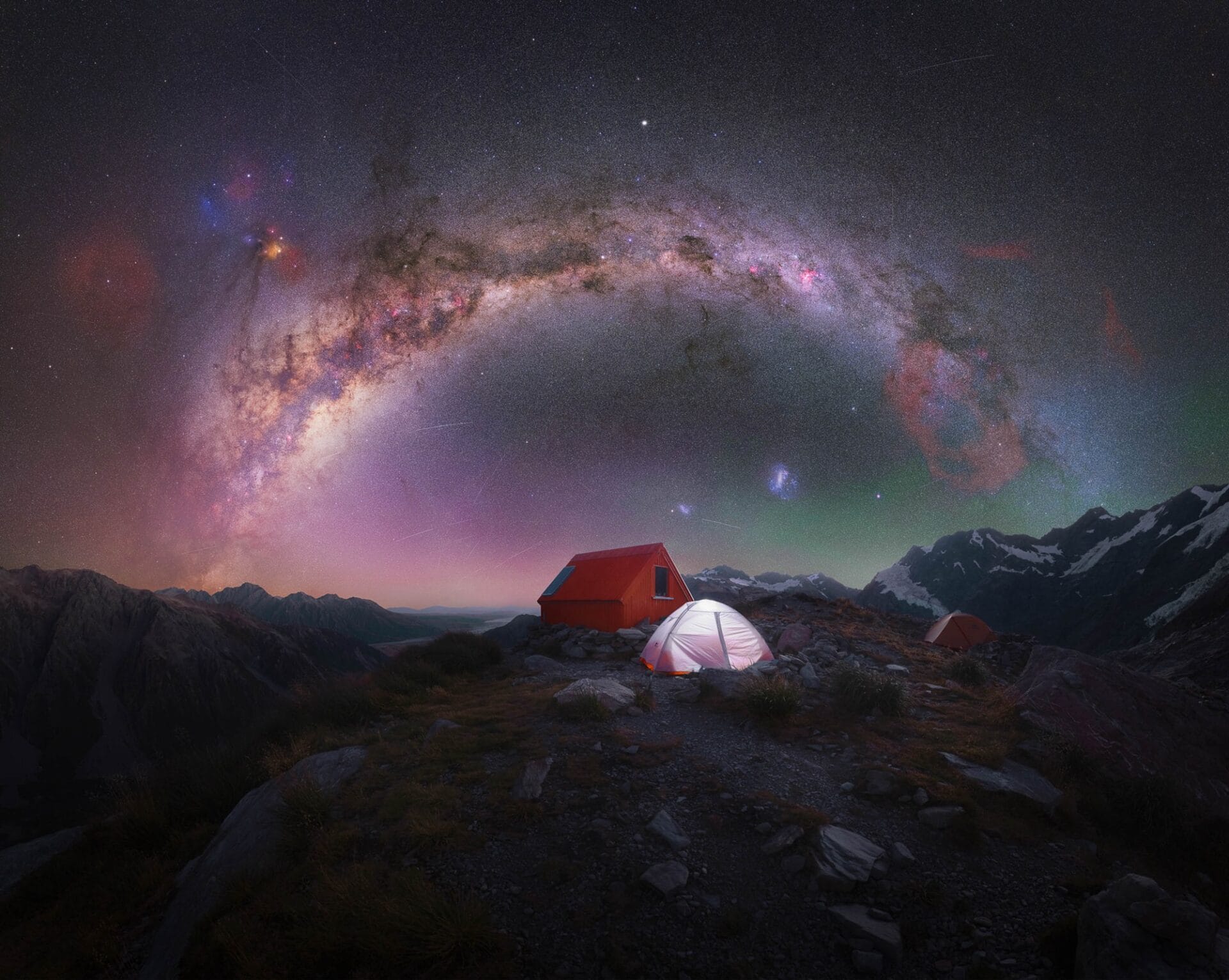 the brilliant star studded milky way above a mountainous landscape with a red shack and tents