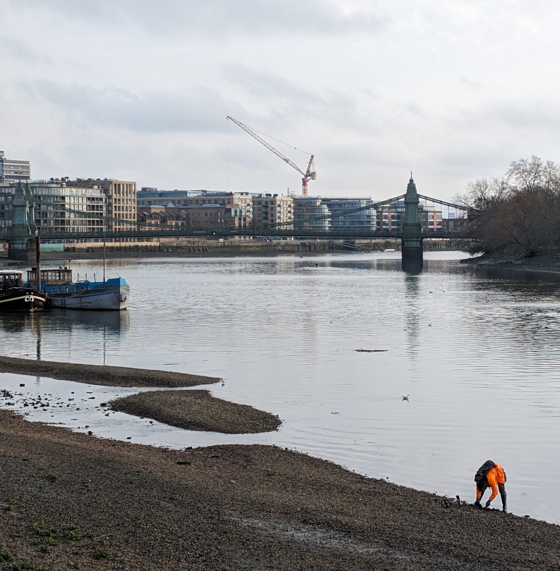 a mudlark sifts through pebbles on the edge of the Thames in London