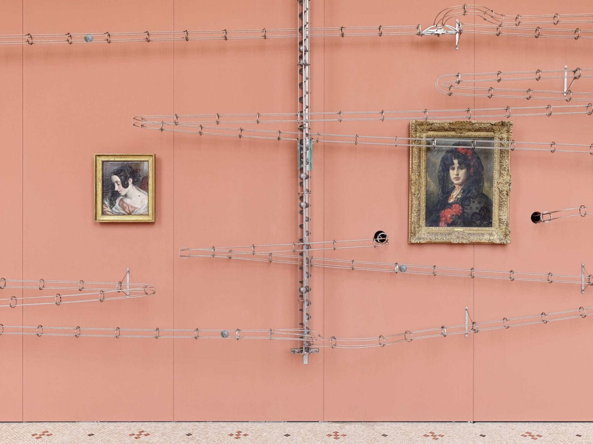 two historic paintings on a pink wall with metal framework and arms reaching across the wall and connecting them or going through holes