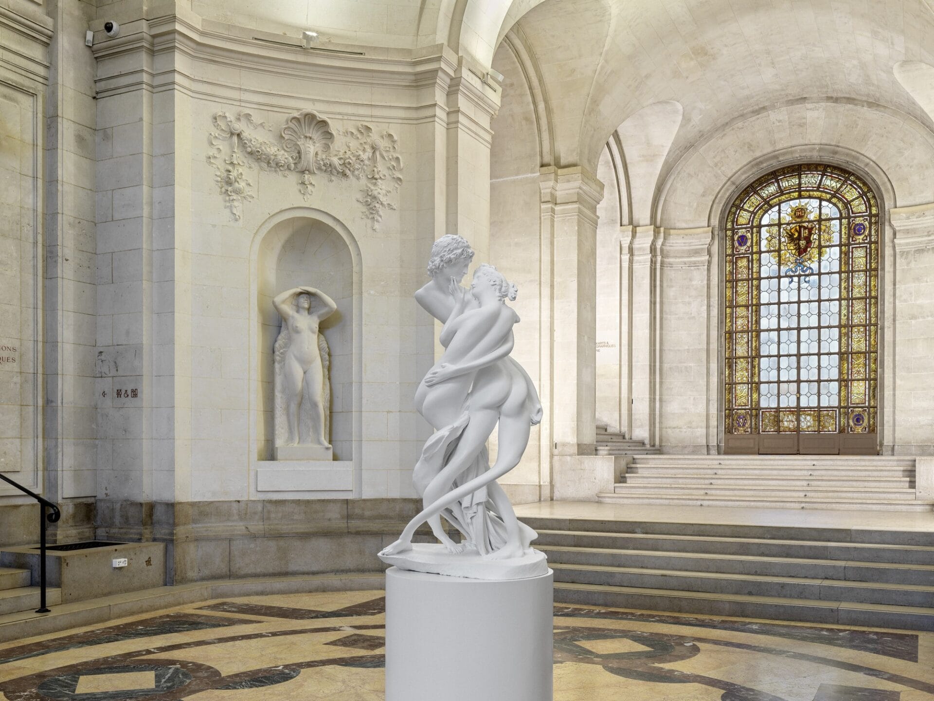 an installation view in a rotunda of a museum with a classical sculpture in a niche in the background and a central sculpture based on a classical piece that has been distorted and elongated