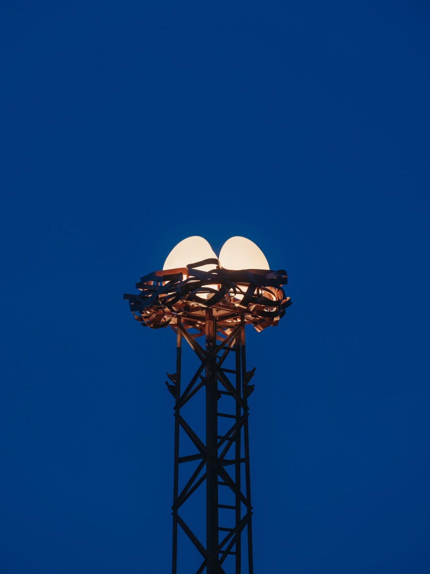 three illuminated eggs perch in a nest atop a tower against a bright blue background