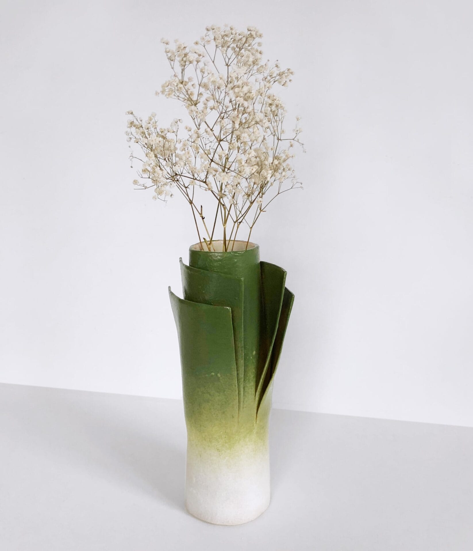 a vase that looks like a cut leek with baby's breath poking from the top