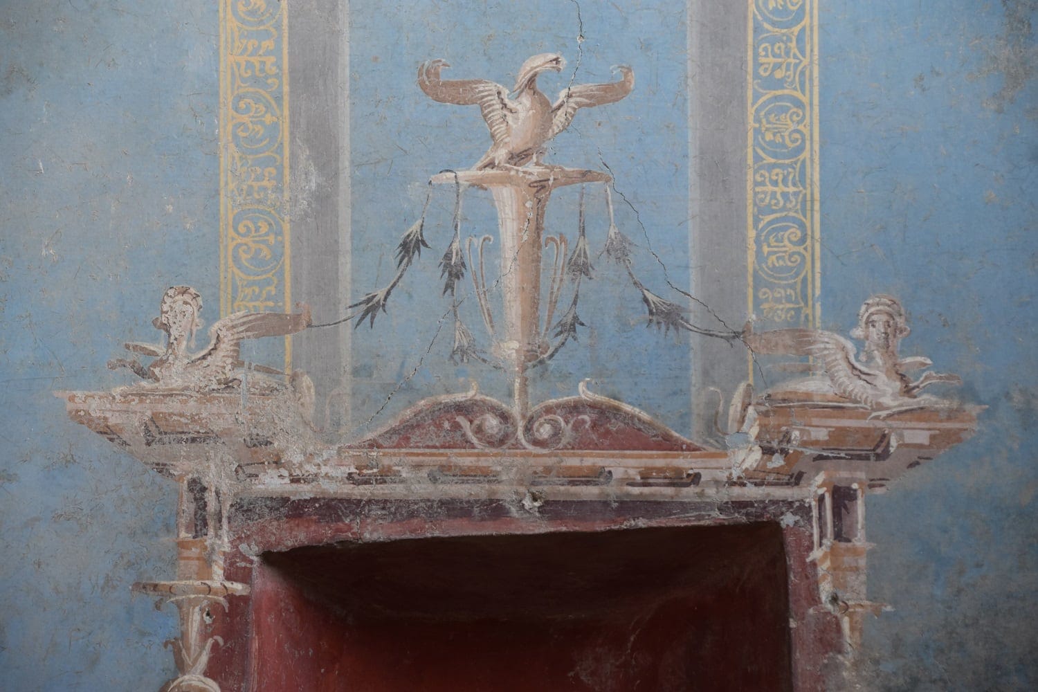 ornate architectural details are painted in a blue fresco surrounding a red niche