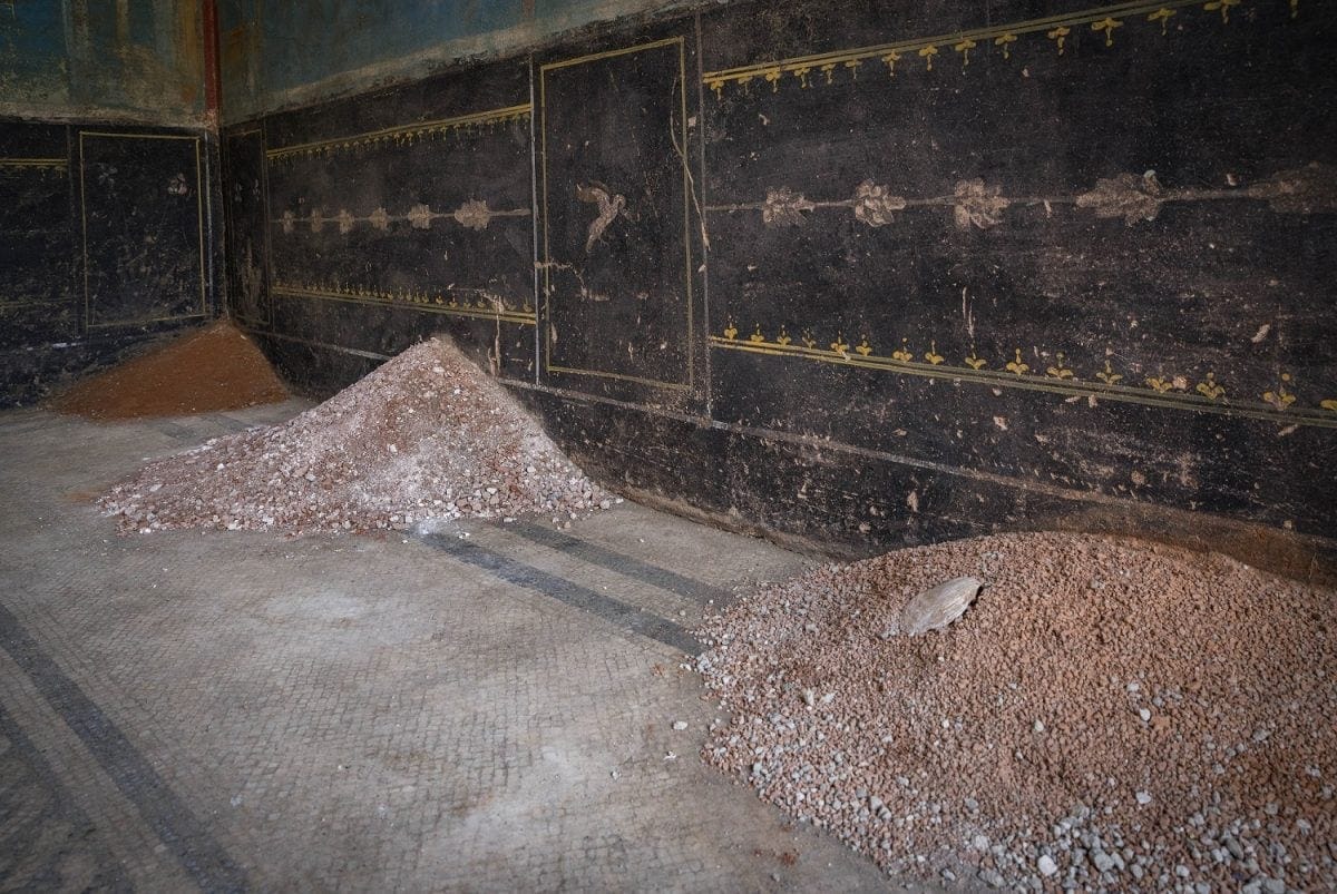 piles of material are on a tiled floor near a black fresco